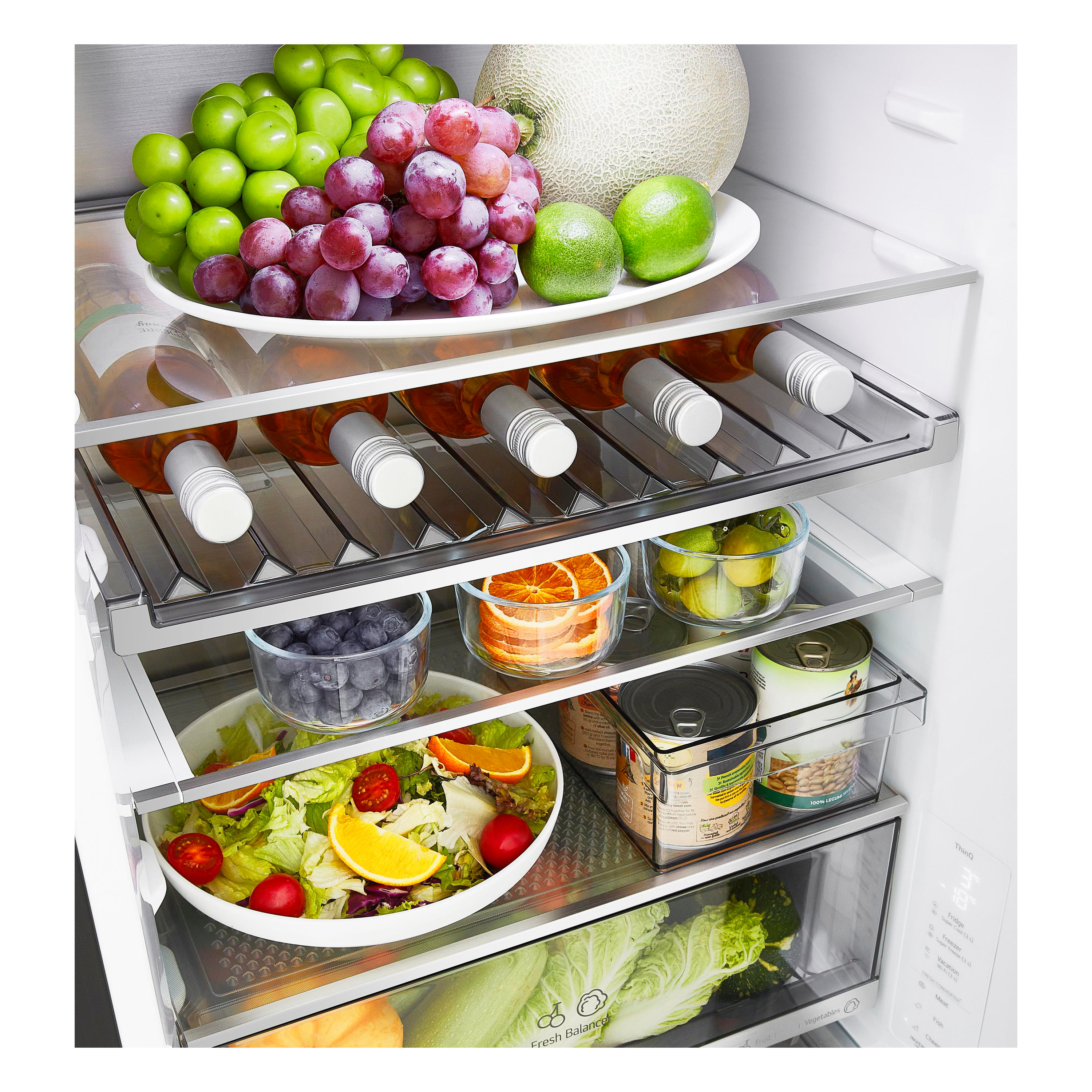 Ein ordentlich gefüllter Kühlschrank mit frischem Obst, Salat, Getränken und Dosen auf den Glasböden.