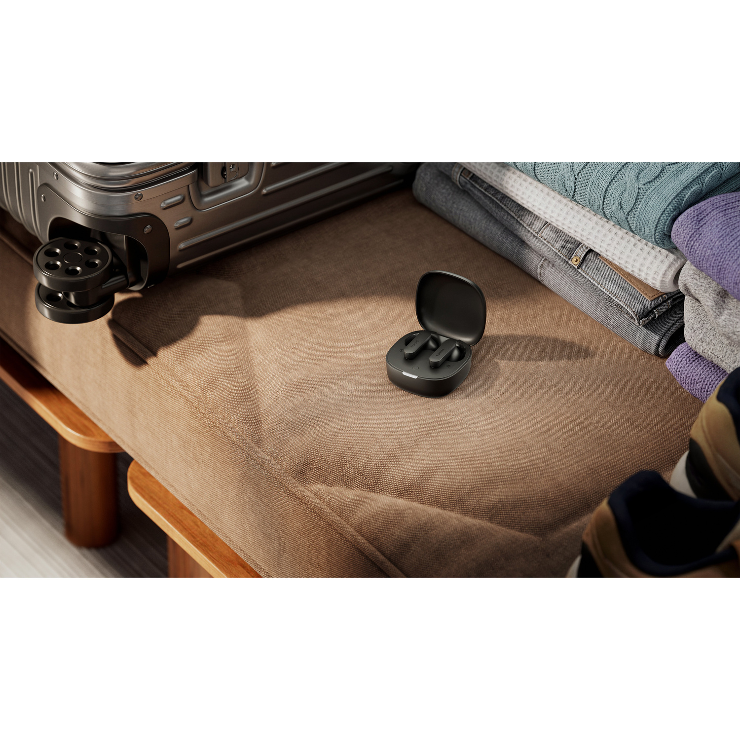 Auricolari wireless neri nella custodia di ricarica su una panca marrone, con valigia e vestiti.