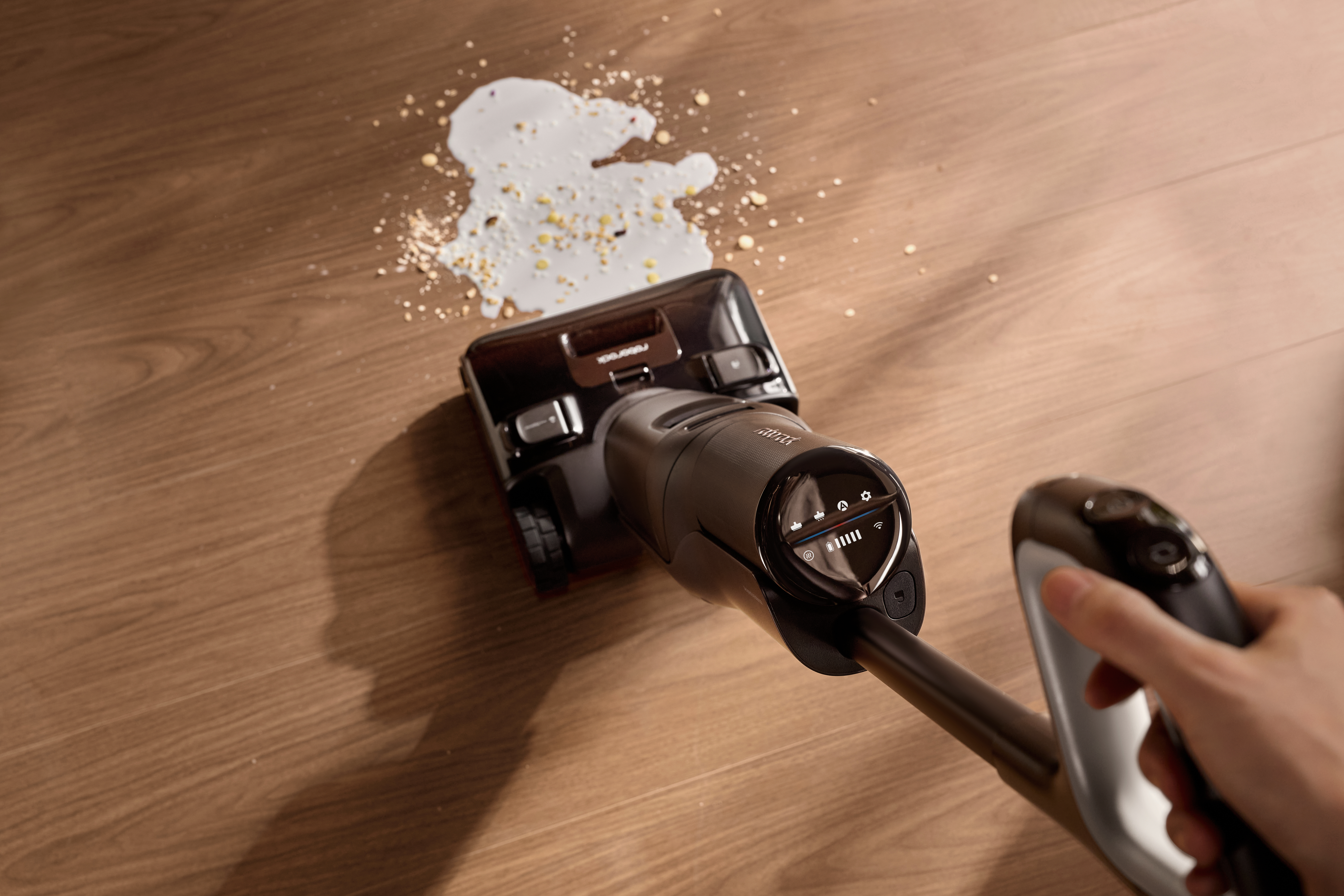 Ein Akkustaubsauger reinigt verschüttete Milch mit Getreide auf einem Holzboden.