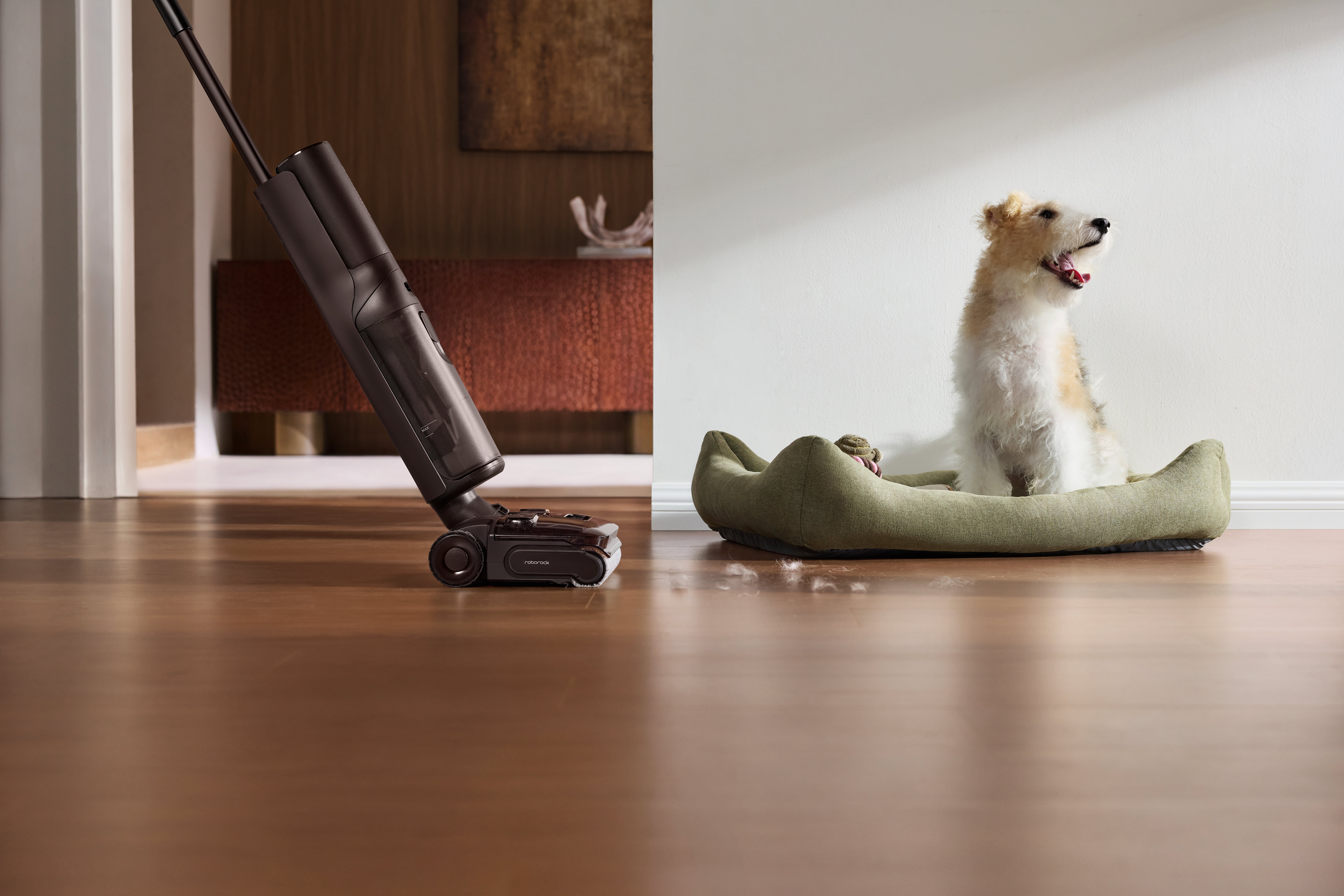 Ein Staubsauger reinigt einen Holzboden, während ein Hund glücklich in seinem Bett sitzt.