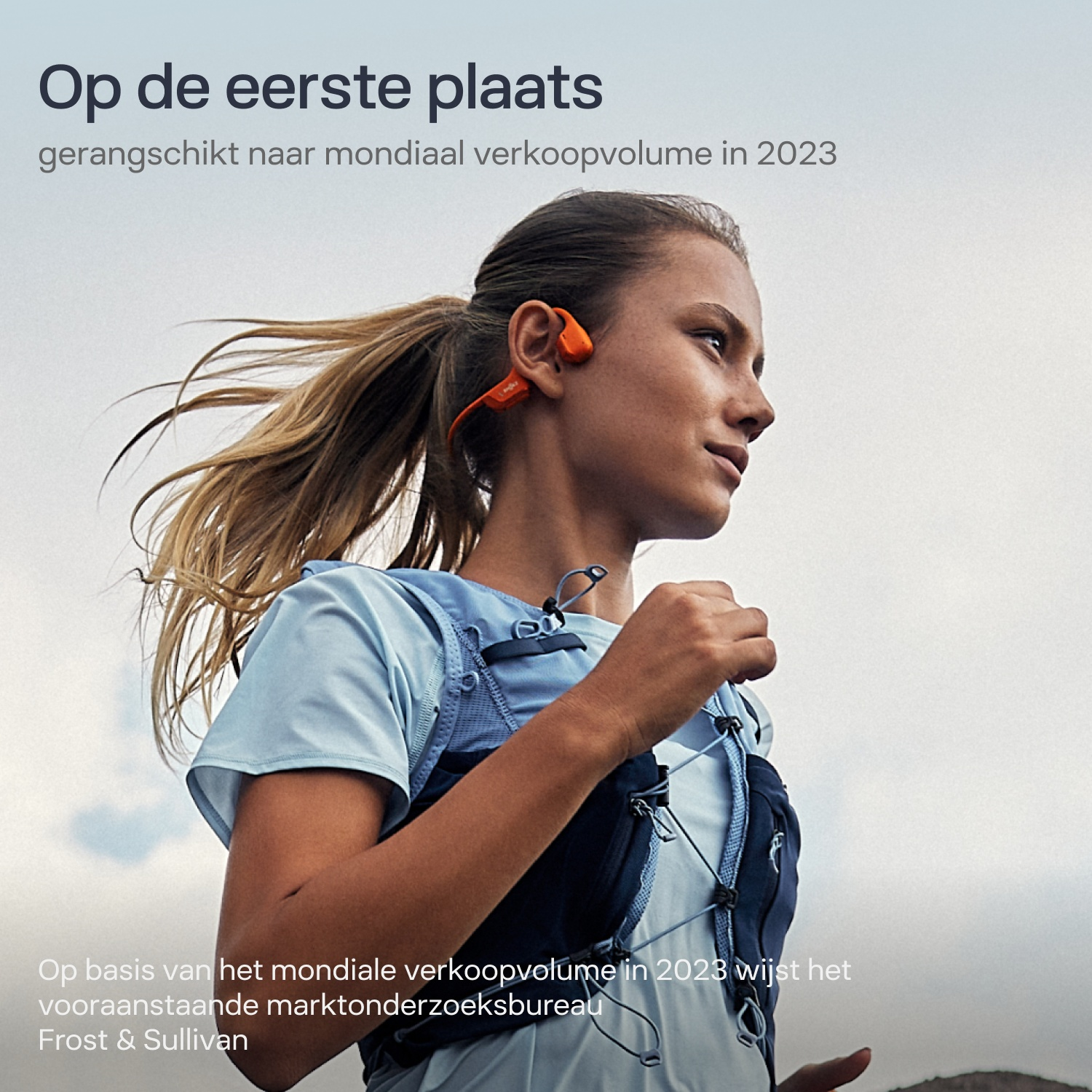 Een vrouw rennend in de buitenlucht met sportkleding, een hardloopvest en oranje koptelefoon.