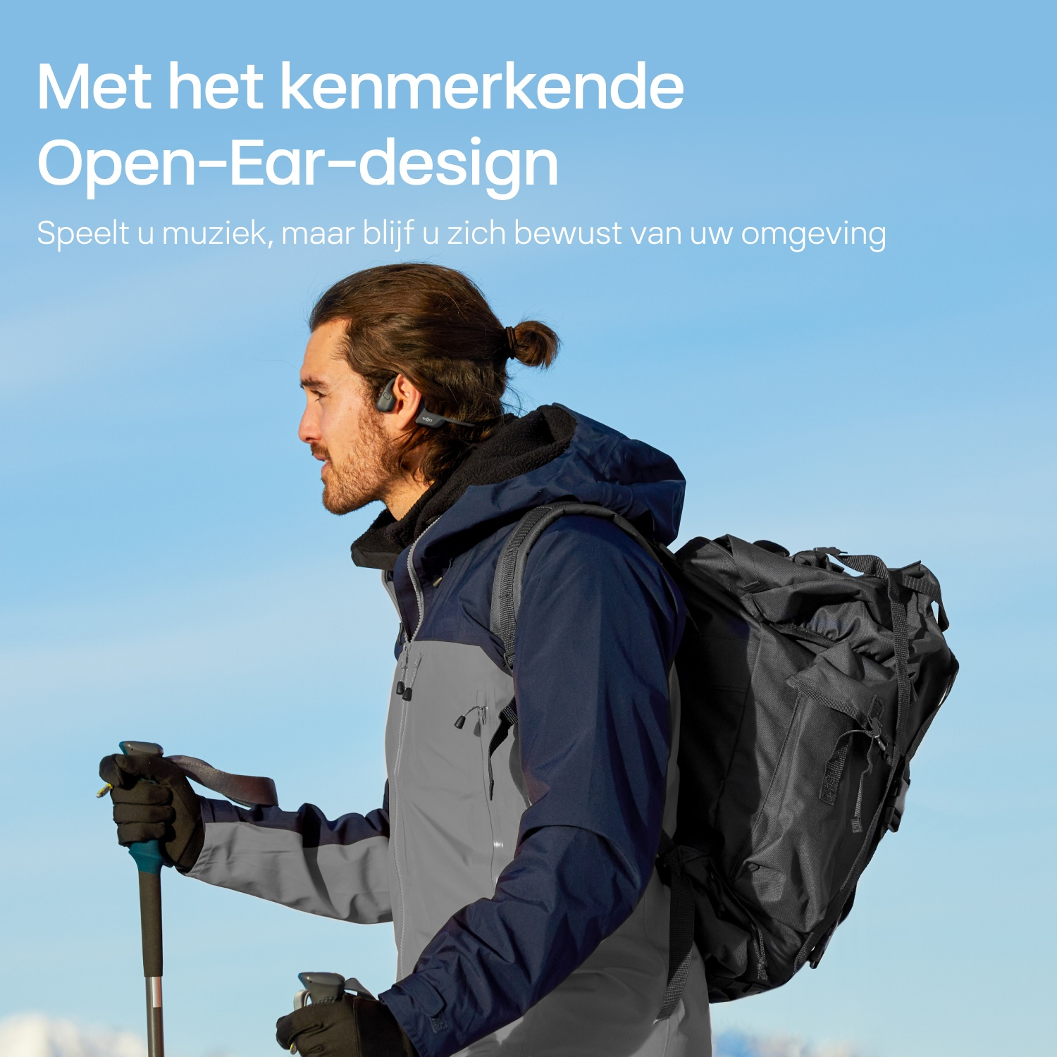 Wandelaar met rugzak en stokken buiten tegen een heldere blauwe lucht.