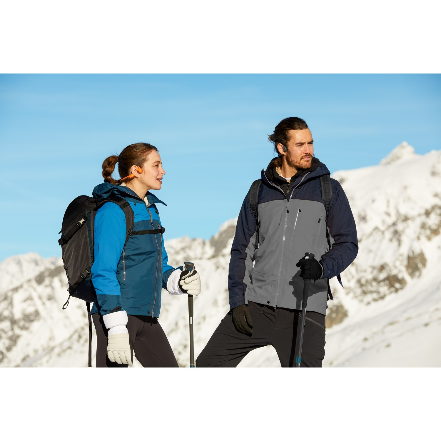 Des randonneurs en vêtements d'hiver avec sacs à dos et bâtons se tiennent devant un décor de montagne enneigée.