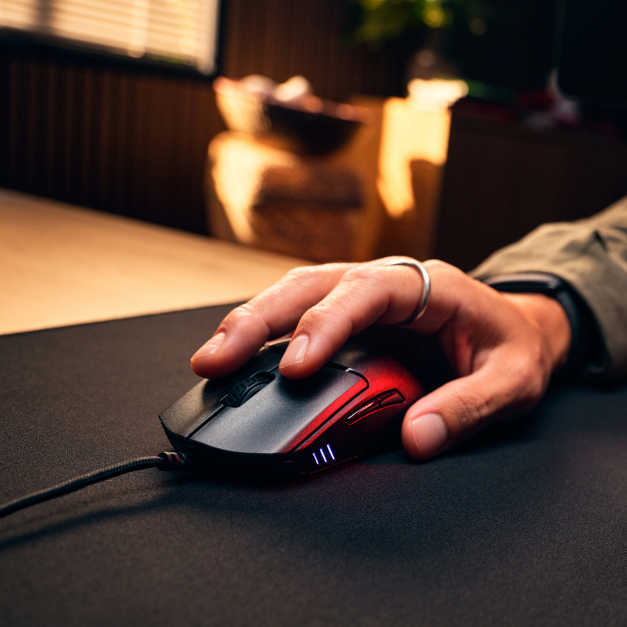 Eine Hand mit silbernem Ring auf einer schwarzen Gaming-Maus mit rotem Licht auf einer schwarzen Matte.