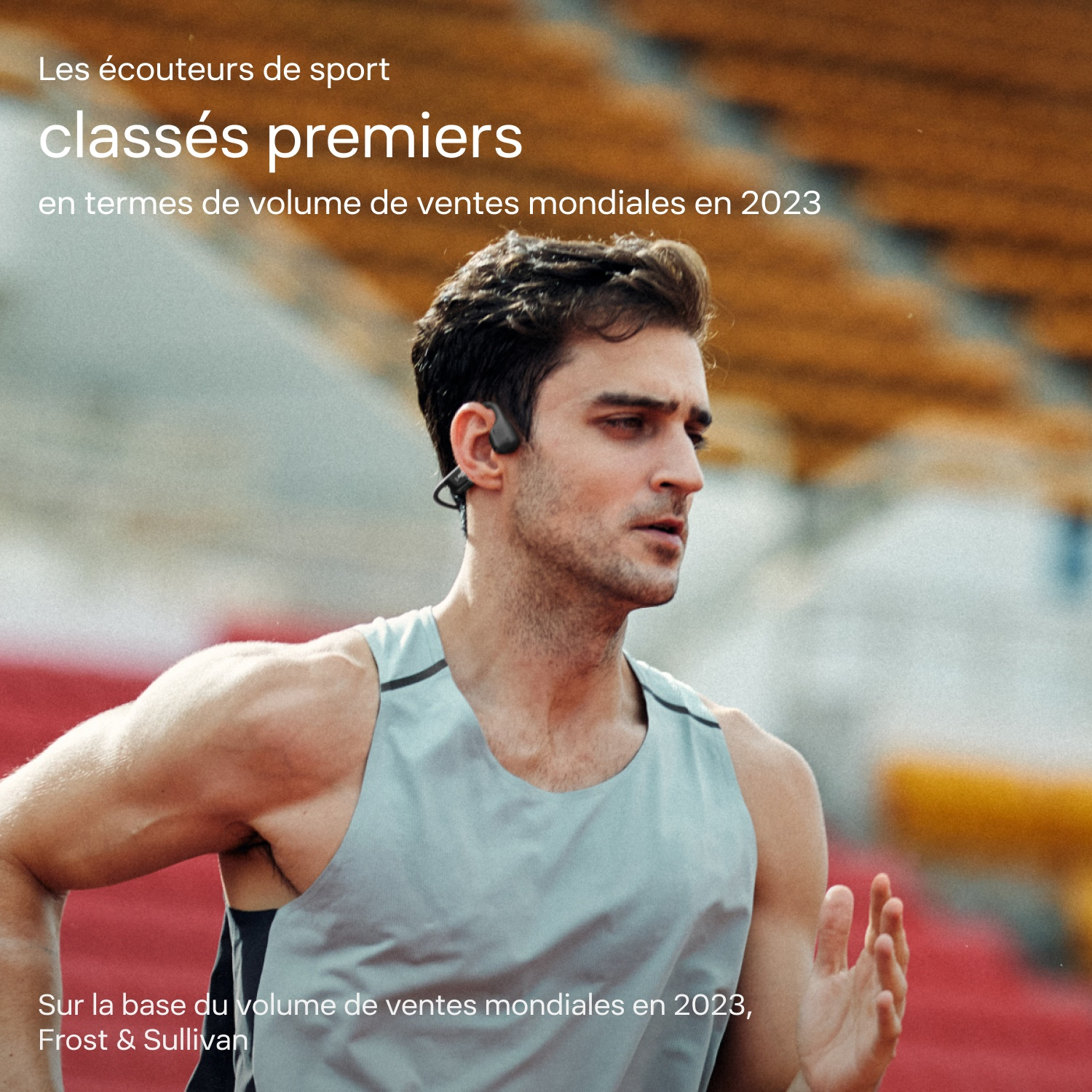 Un athlète en débardeur gris court devant des tribunes de stade rouges et oranges.