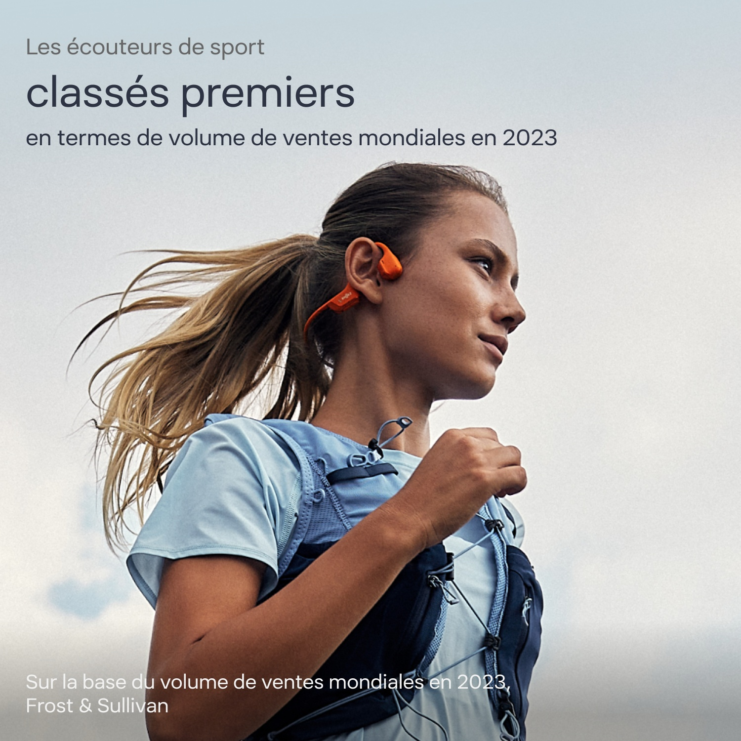 Une coureuse blonde avec des écouteurs à conduction osseuse orange portant un texte publicitaire.