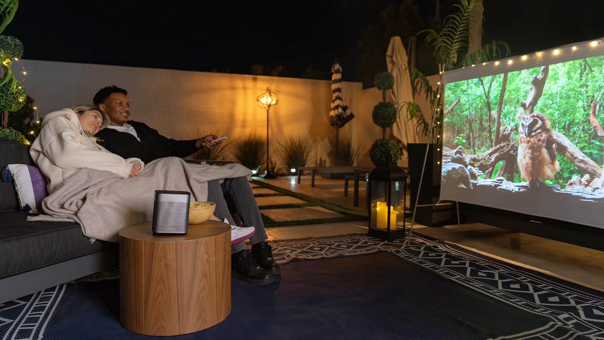 Çift gece dışarıda bir kanepeden projektör ekranında film izliyor.