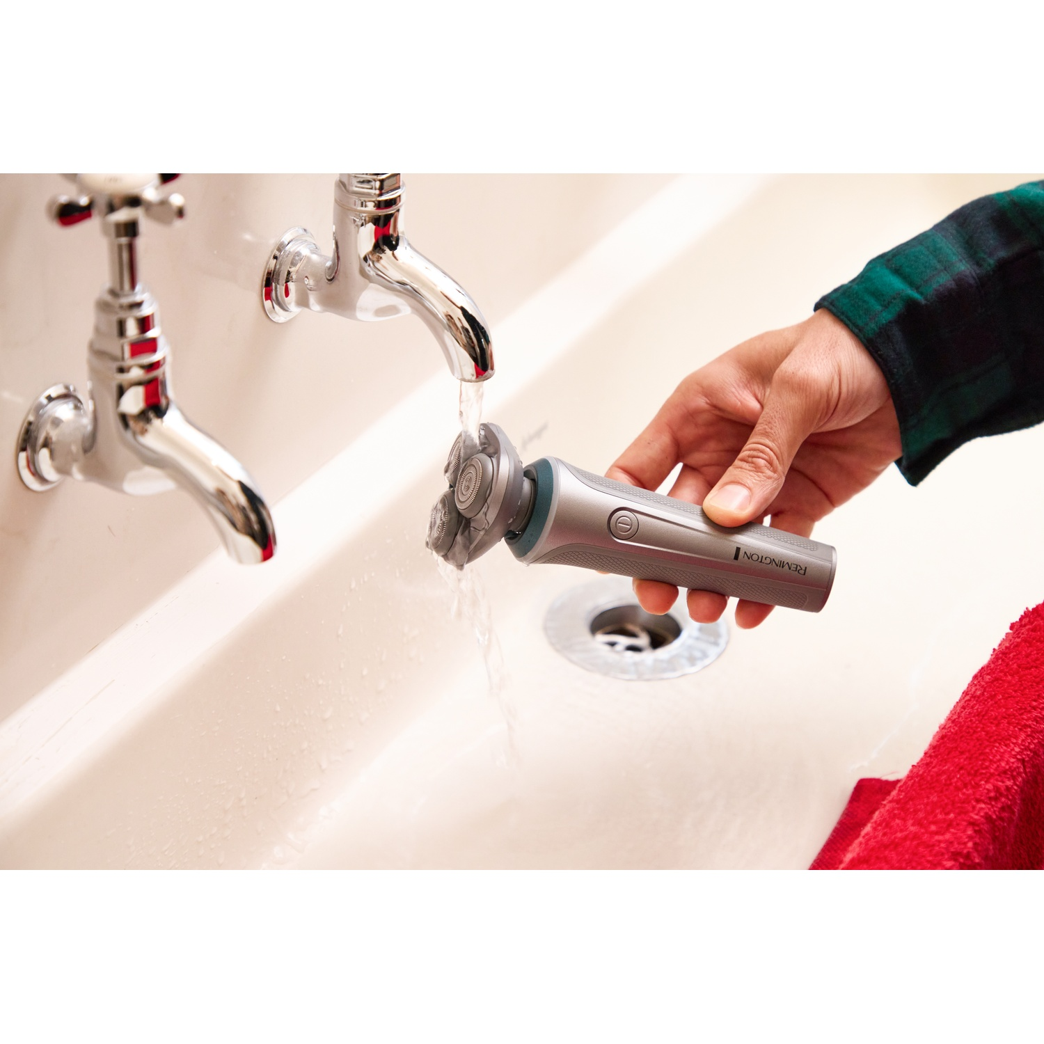 Een hand houdt een grijs Remington-scheerapparaat onder stromend water uit een wastafelkraan.