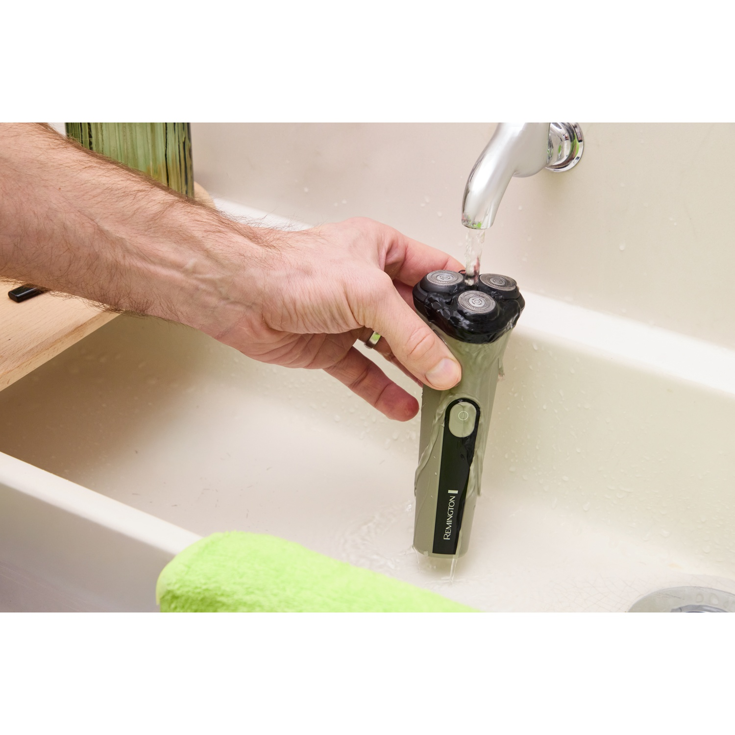 Een hand houdt een Remington-scheerapparaat onder stromend water in een wasbak.