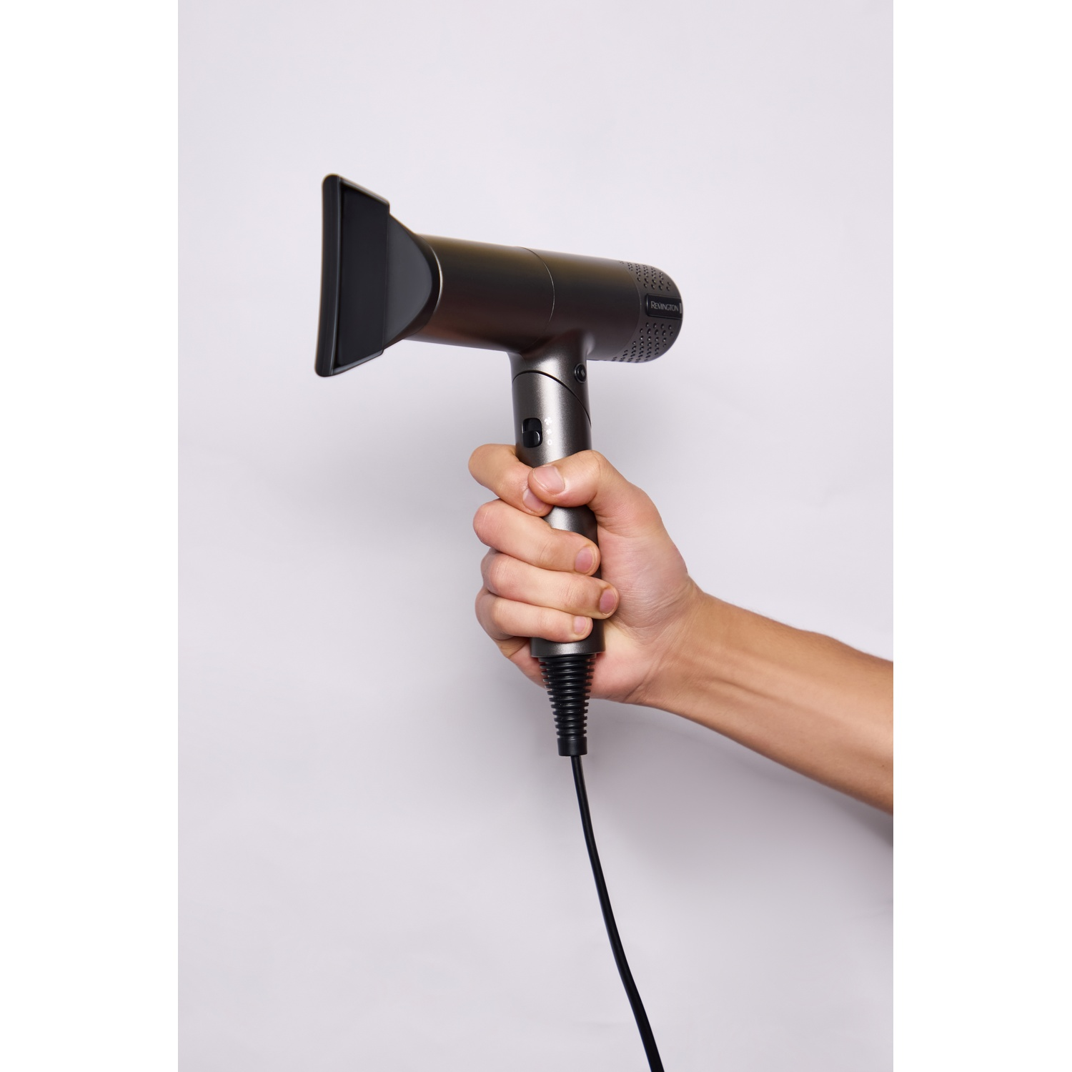 Een hand houdt een grijze haardroger met zwart mondstuk en snoer tegen een witte achtergrond.