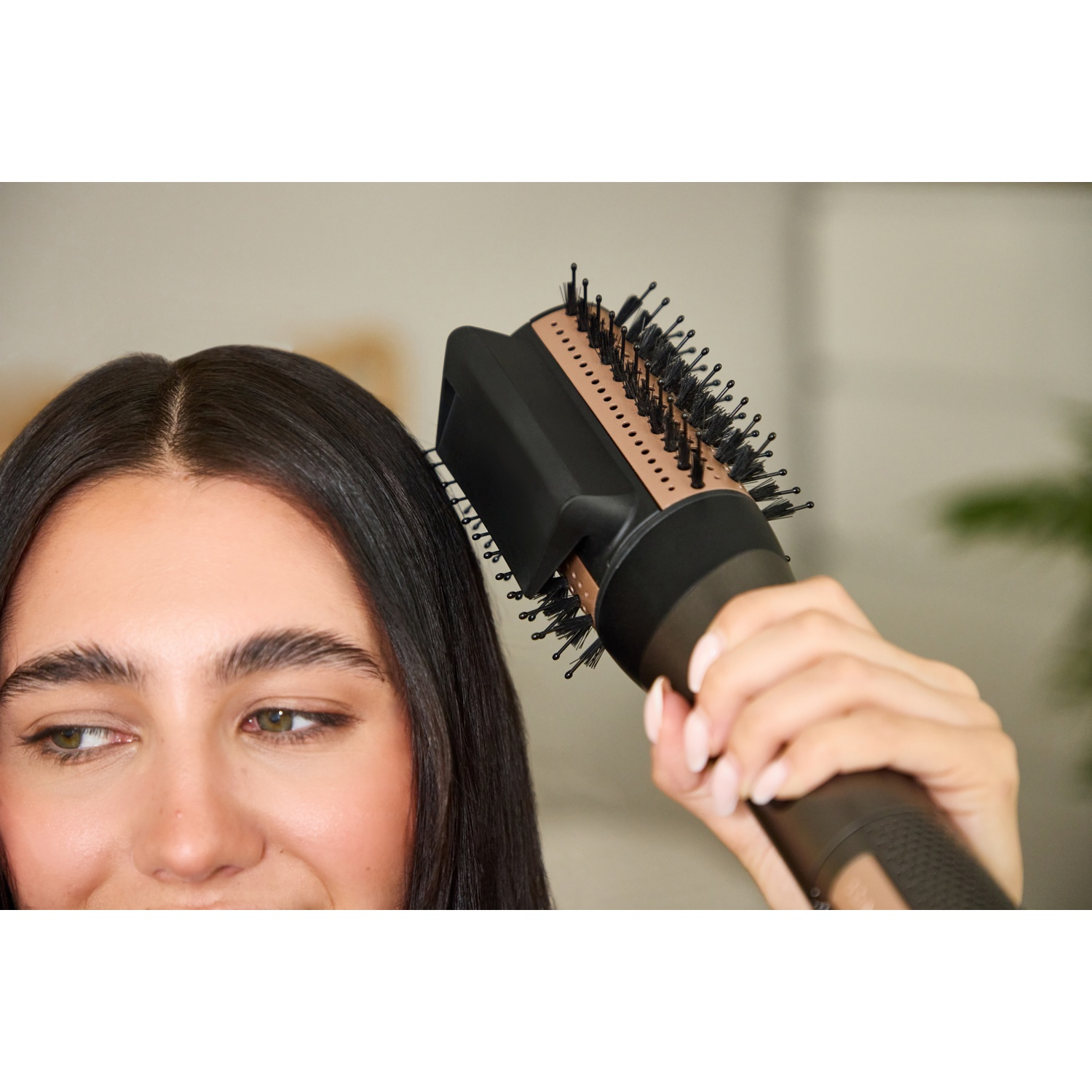 Une femme coiffe ses longs cheveux sombres avec une brosse soufflante noire et or rose.