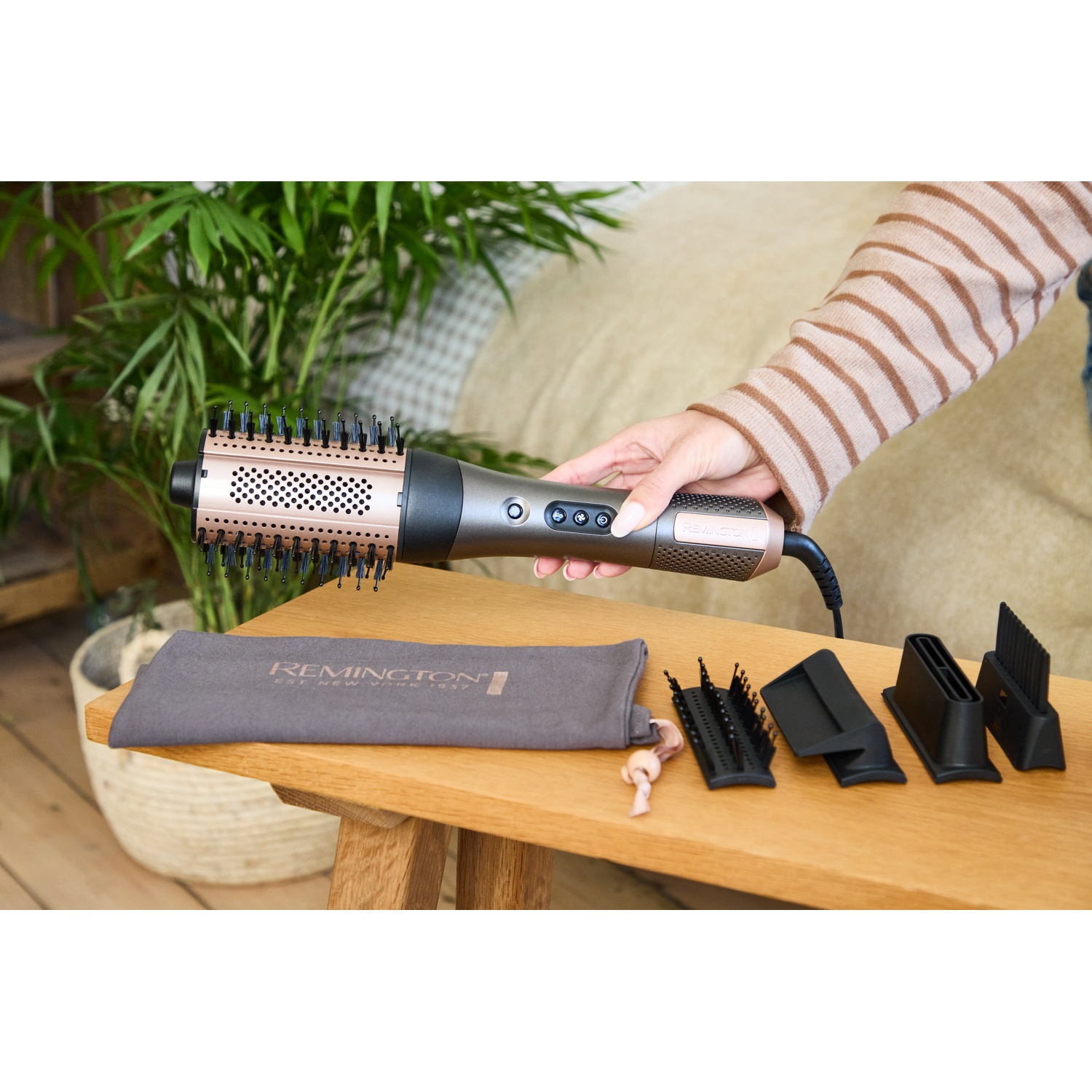 Personne tenant une brosse soufflante Remington avec des accessoires sur une table.