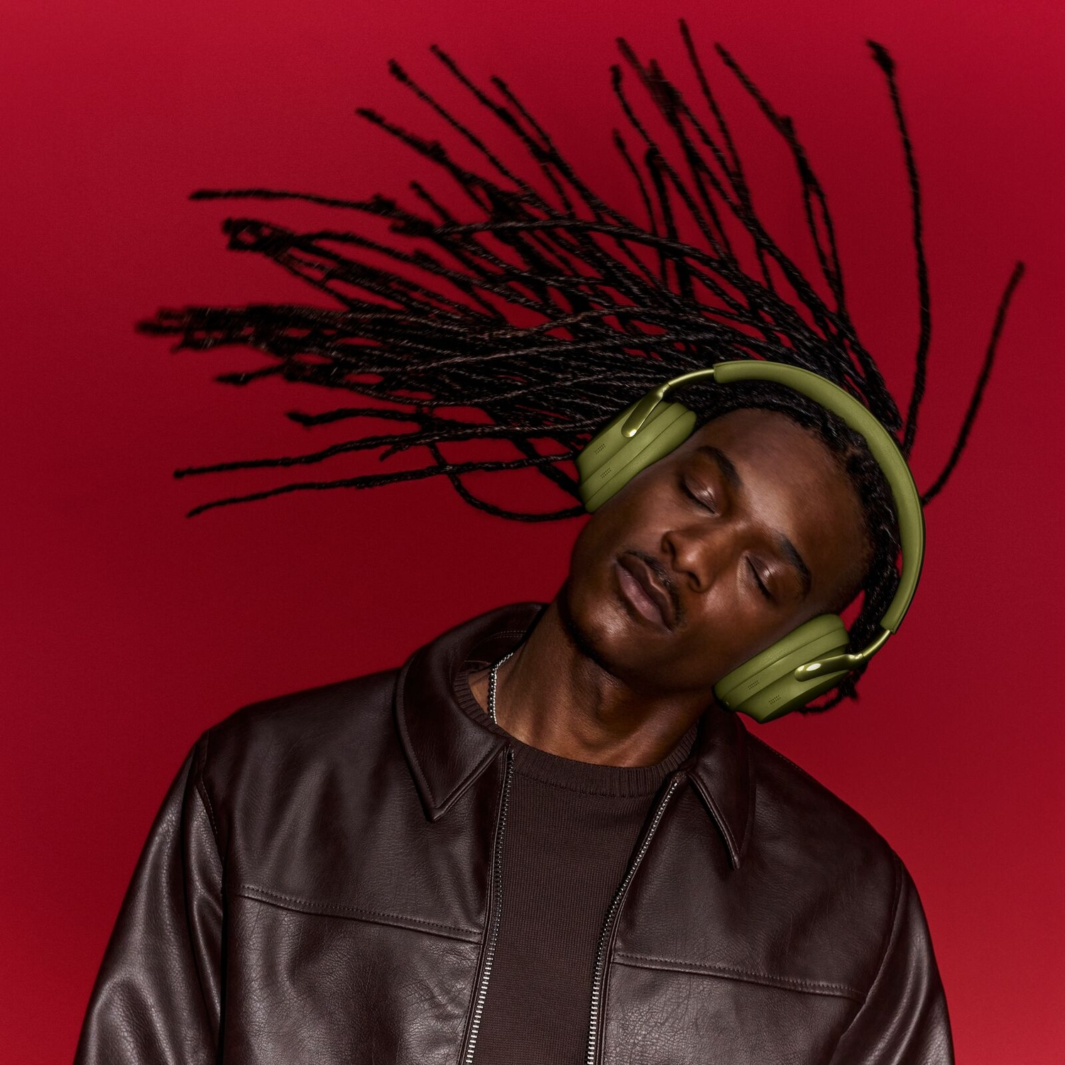 A man with green headphones and dreadlocks tosses his head back against a red background.