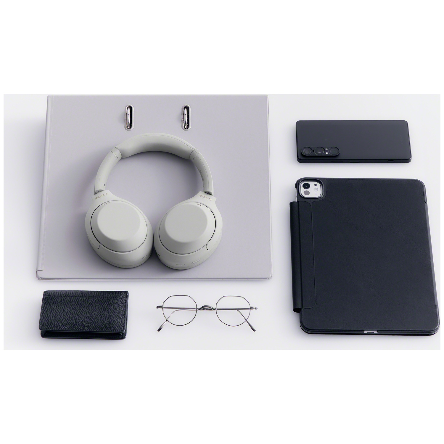 A folder, light headphones, black wallet, glasses, smartphone, and tablet arranged on a white surface.