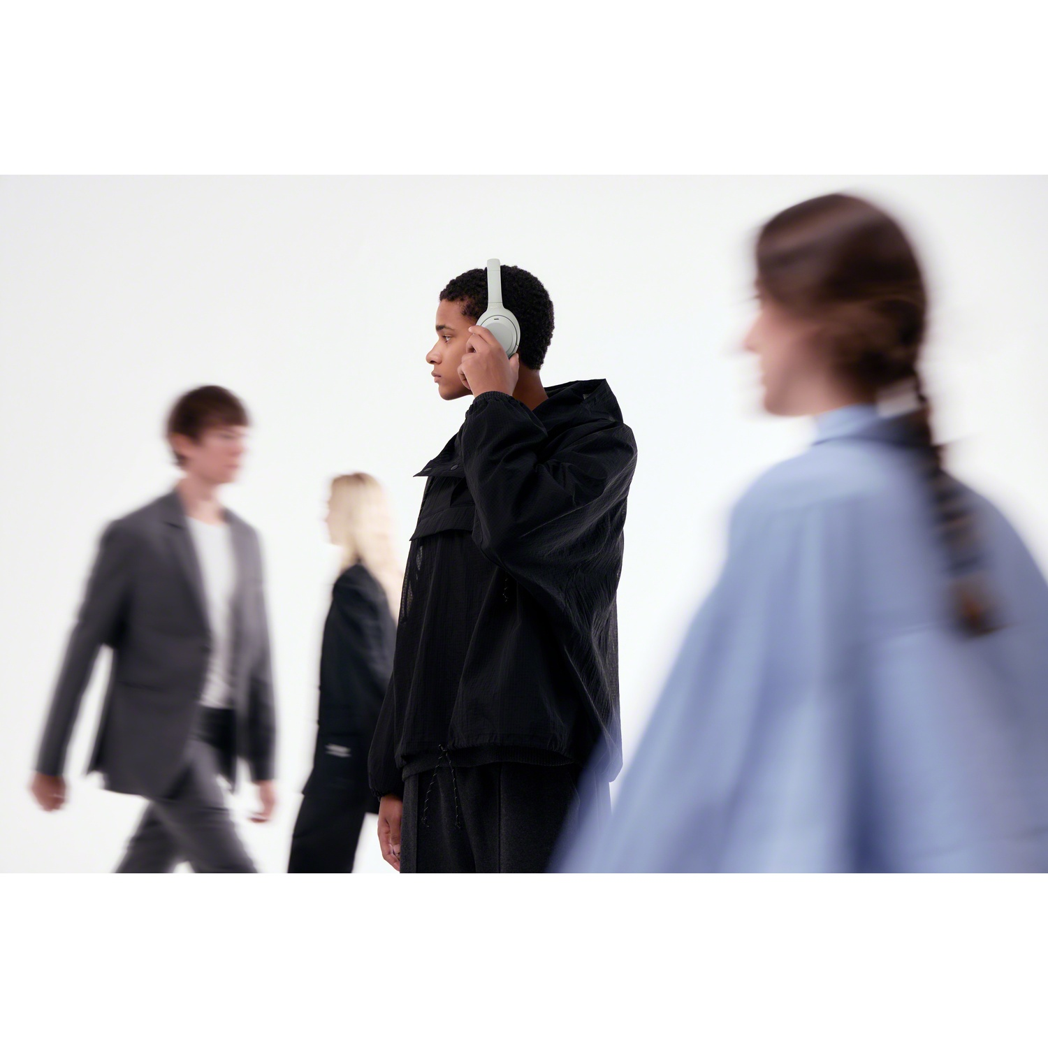 A young man wearing headphones is in focus while other people walk past blurred.