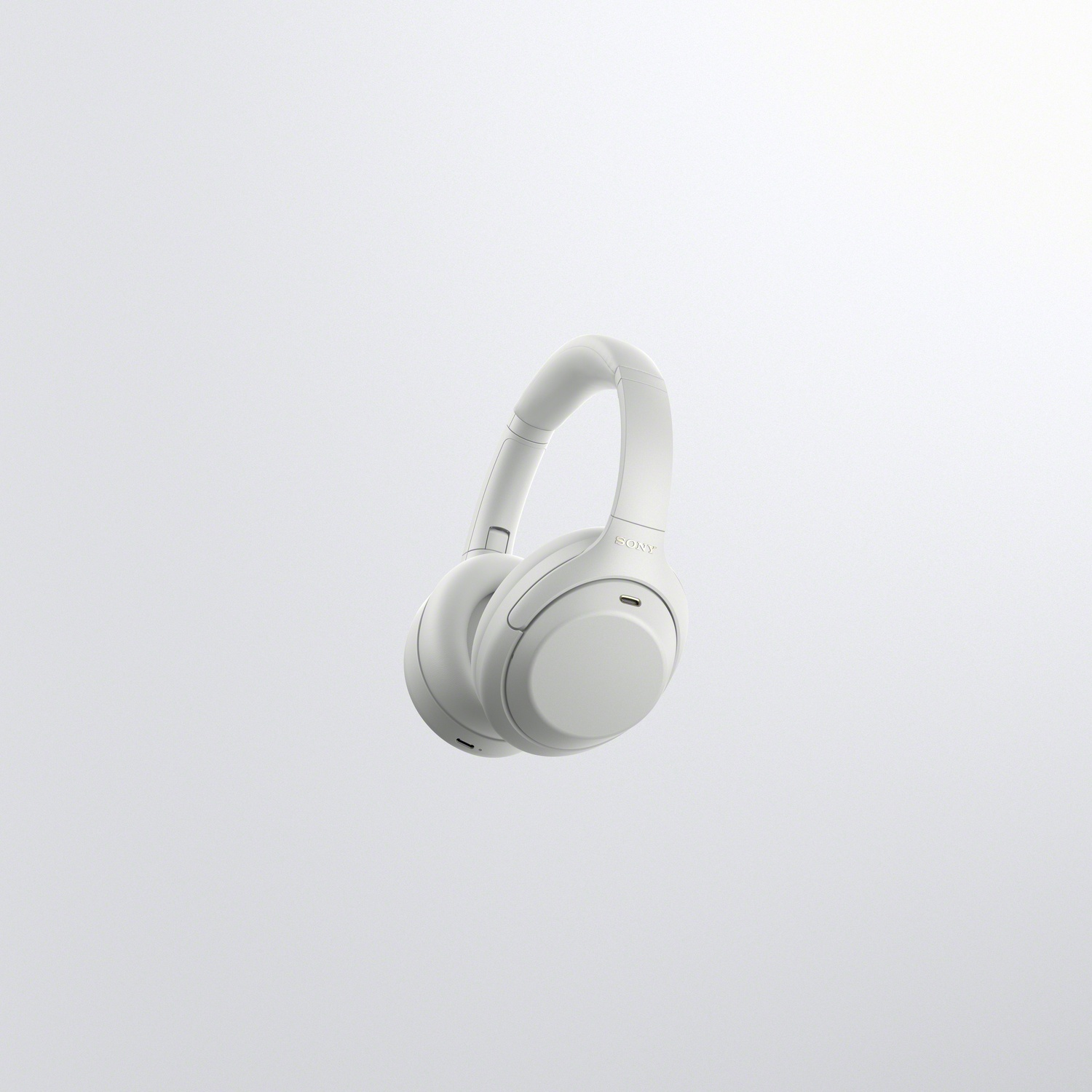 White wireless Sony over-ear headphones floating against a plain light gray background.