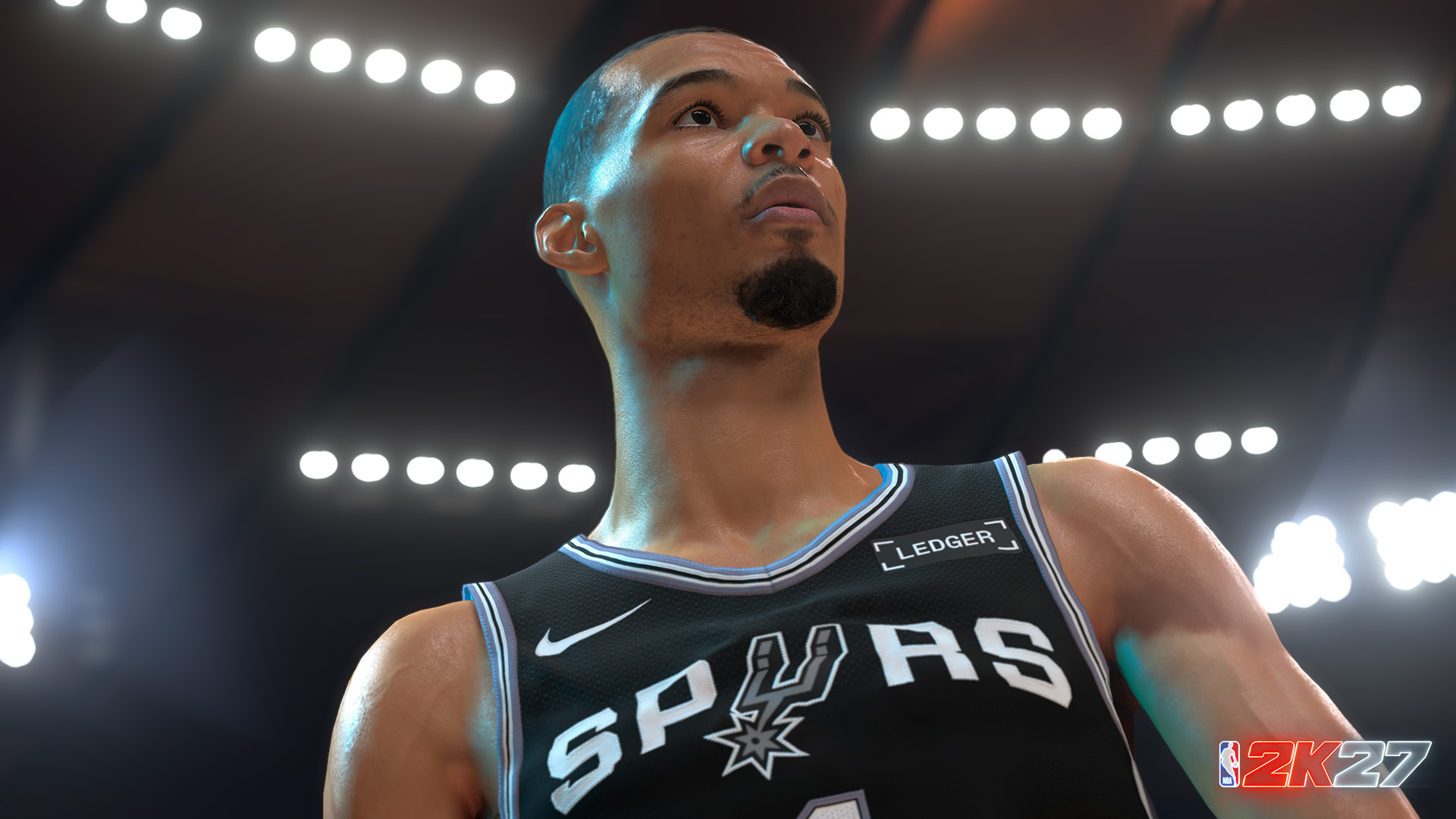 Siyah Spurs forması giyen bir basketbol oyuncusu, parlak ışıklı bir arenada yukarı bakıyor.
