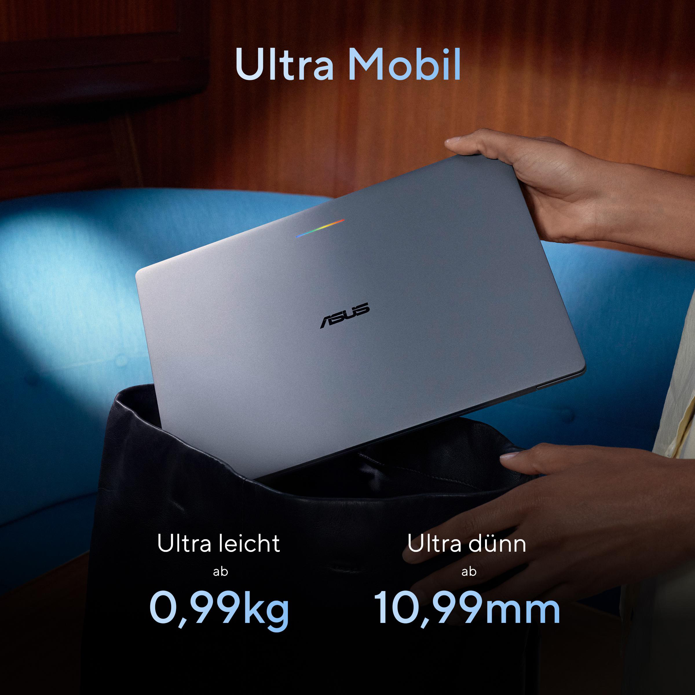 Eine Person legt einen schmalen grauen Asus Laptop in eine schwarze Tasche vor blauem Hintergrund.