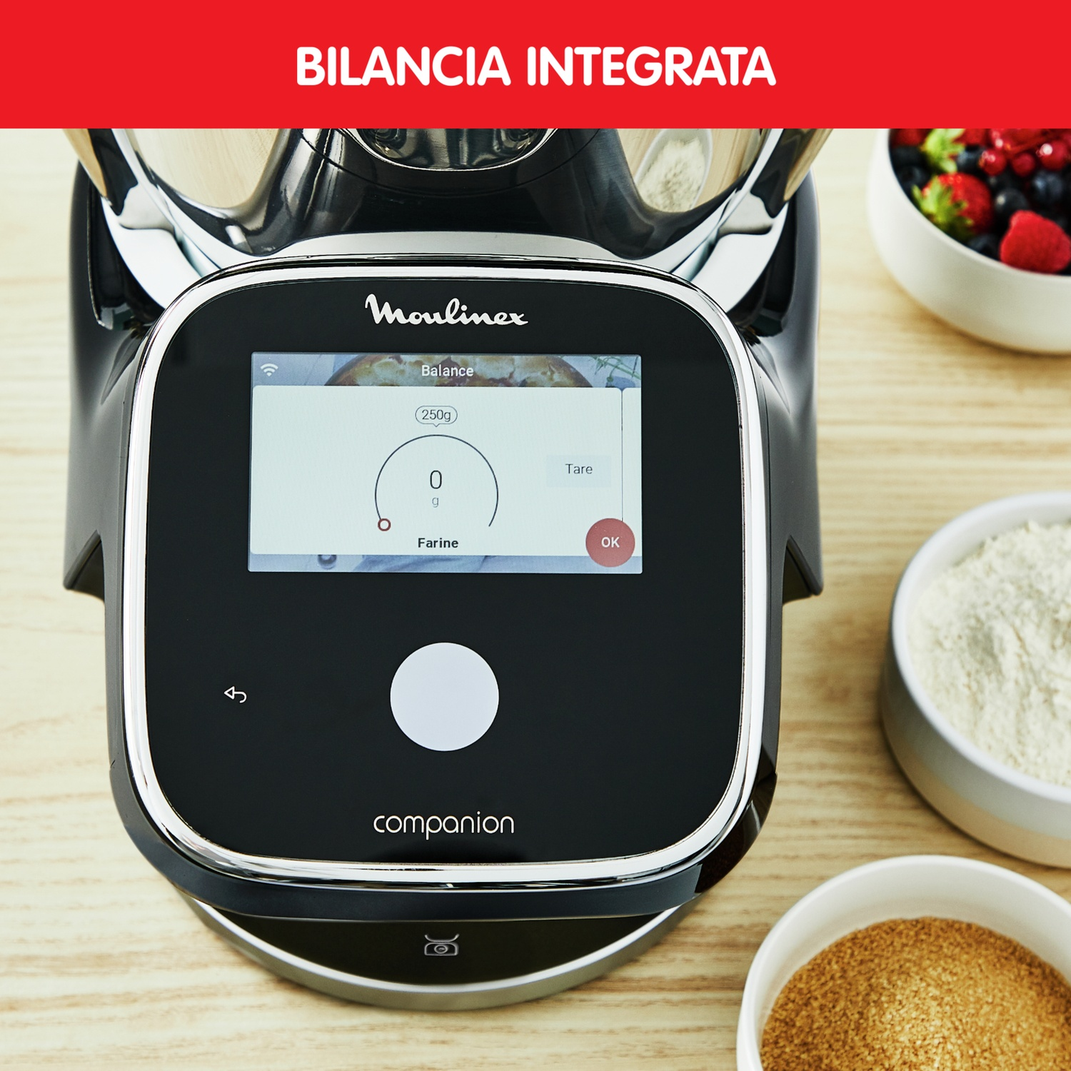 Robot da cucina Moulinex con bilancia digitale e ciotole di farina, zucchero e bacche su legno.