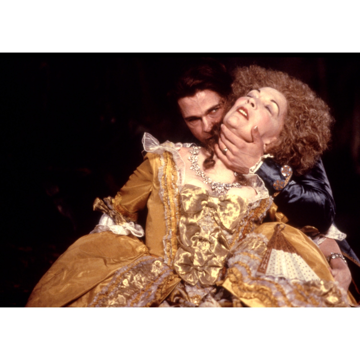 Un vampire en costume d'époque mord le cou d'une femme portant une robe dorée.