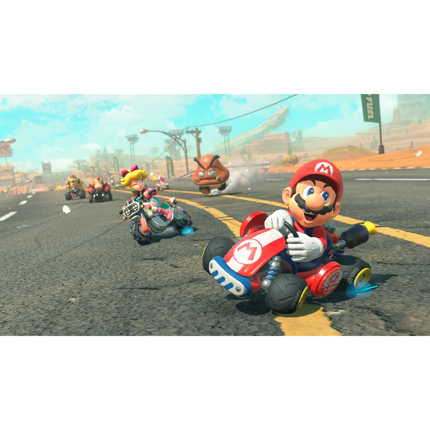 Mario rijdt in zijn rode kart over een zonnige woestijnweg, gevolgd door Peach op een motor.
