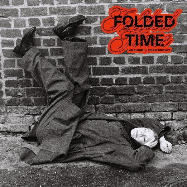 Eine Person liegt vor einer Backsteinwand, Beine und Arme angewinkelt, darüber der rote Schriftzug Folded Time.