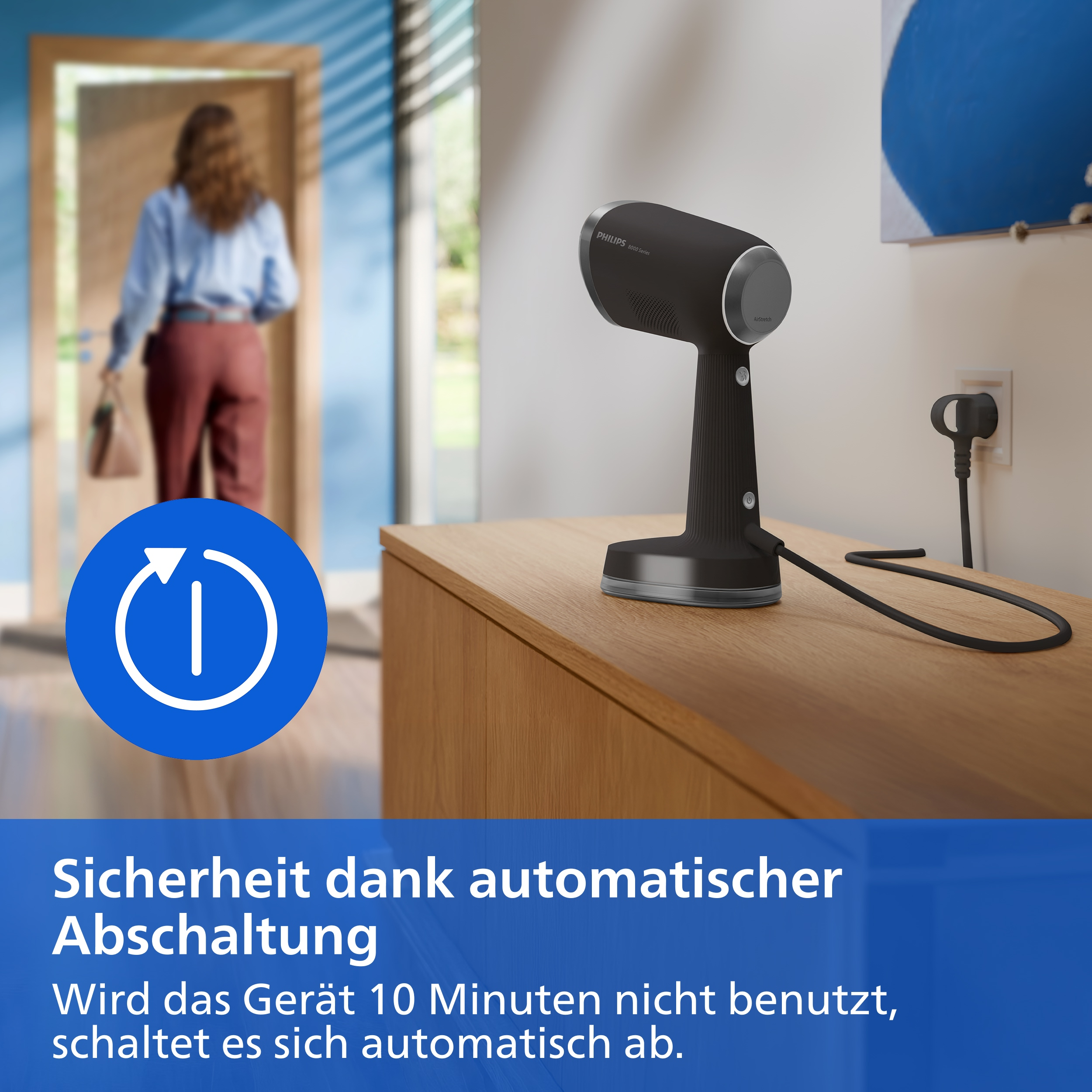 Ein schwarzer Philips Airstretch Haartrockner steht auf einer Holzkommode, während im Hintergrund eine Frau durch eine Tür geht.