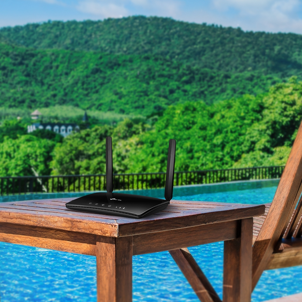 Ein schwarzer WLAN-Router auf einem Holztisch vor einem Pool und bewaldeten Bergen.