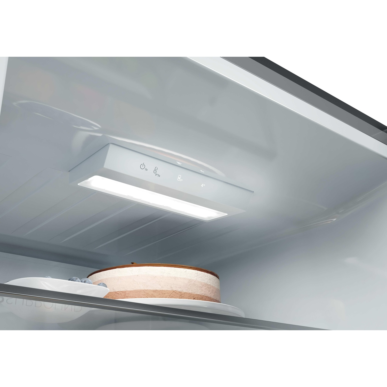 Vue intérieure d'un réfrigérateur avec éclairage LED, commandes intégrées, gâteau et myrtilles sur une étagère.