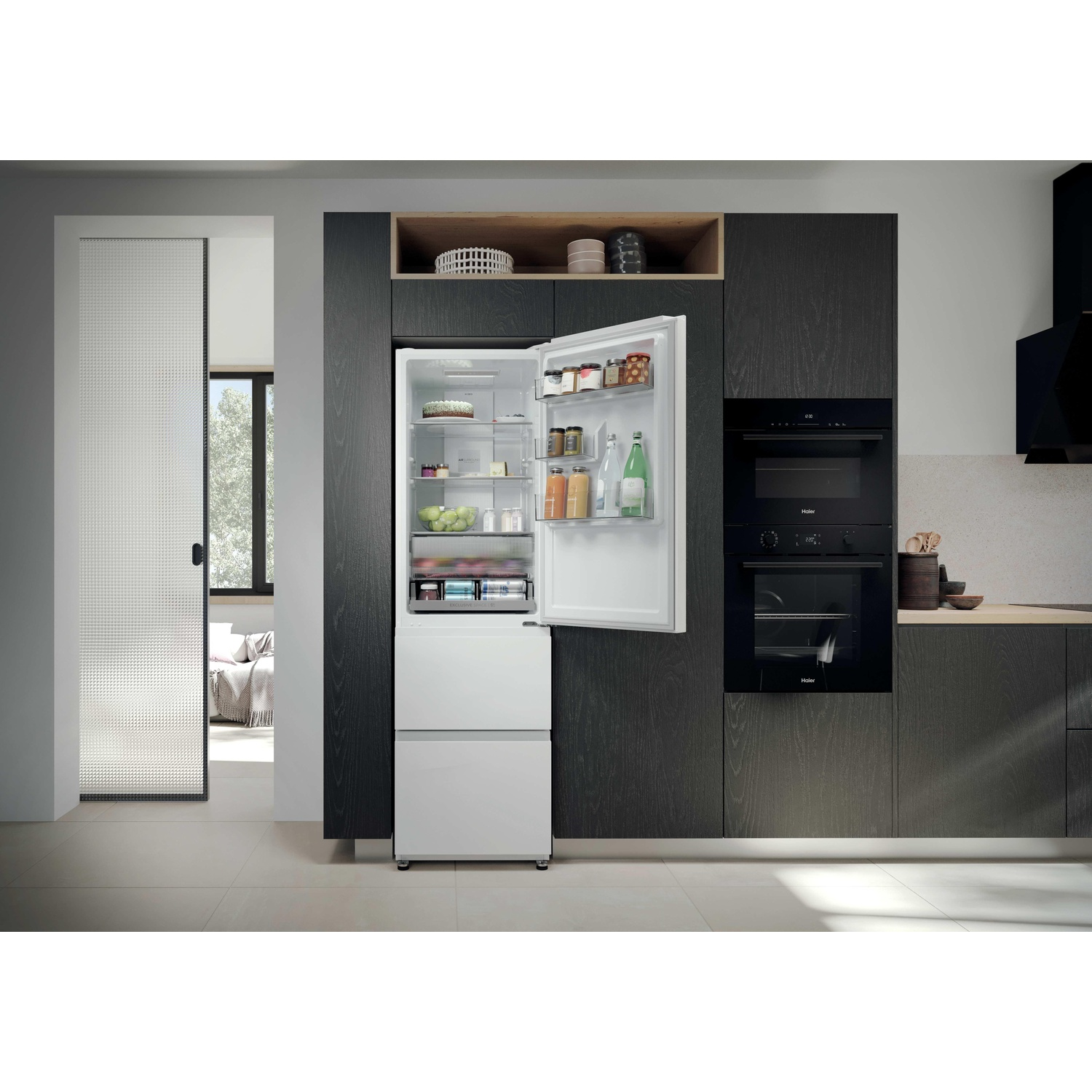 Cuisine moderne avec réfrigérateur blanc intégré, porte ouverte, placards sombres et fours encastrés.