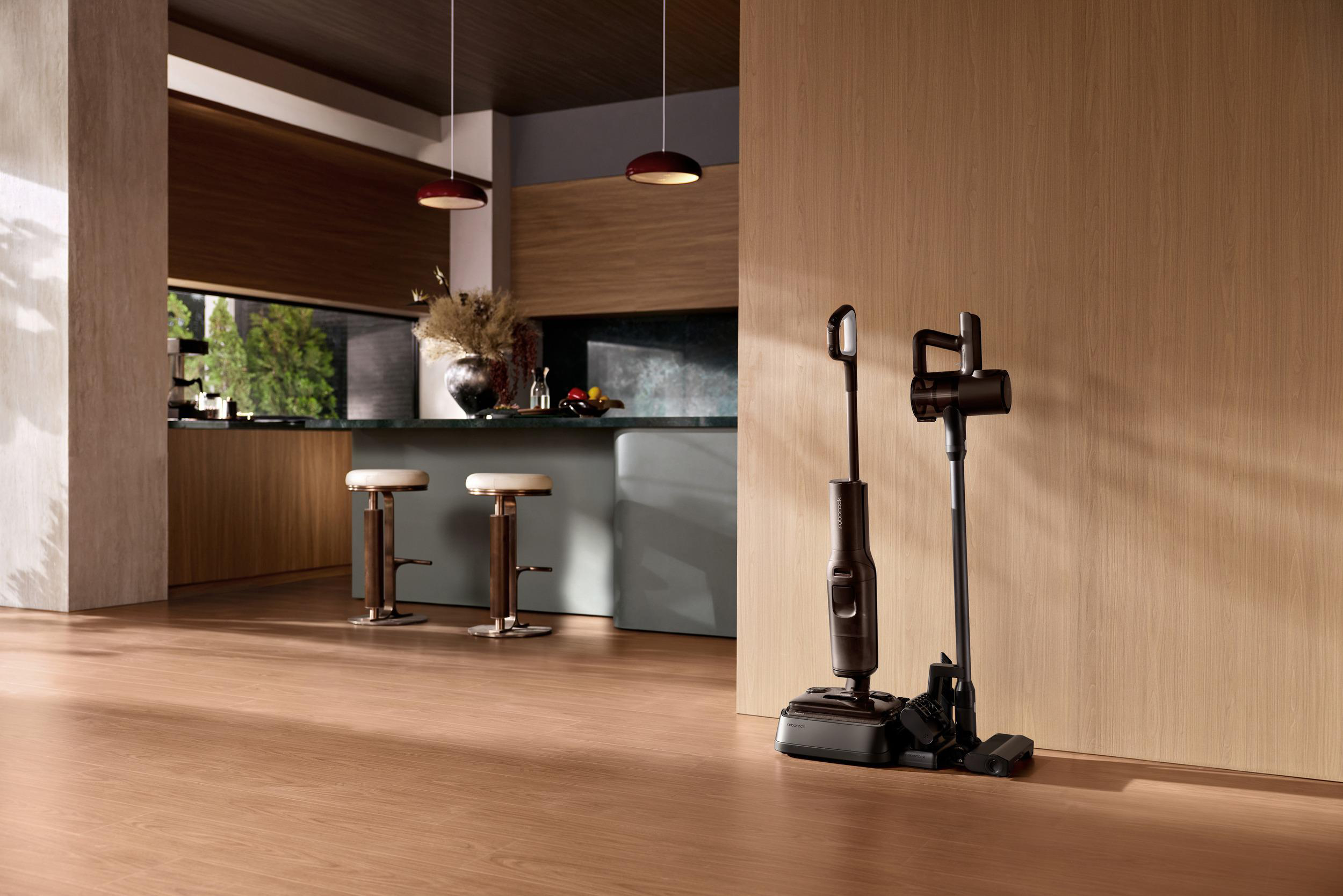 Zwei dunkle Staubsauger stehen auf einem Holzboden in einem modernen Raum mit Küche im Hintergrund.