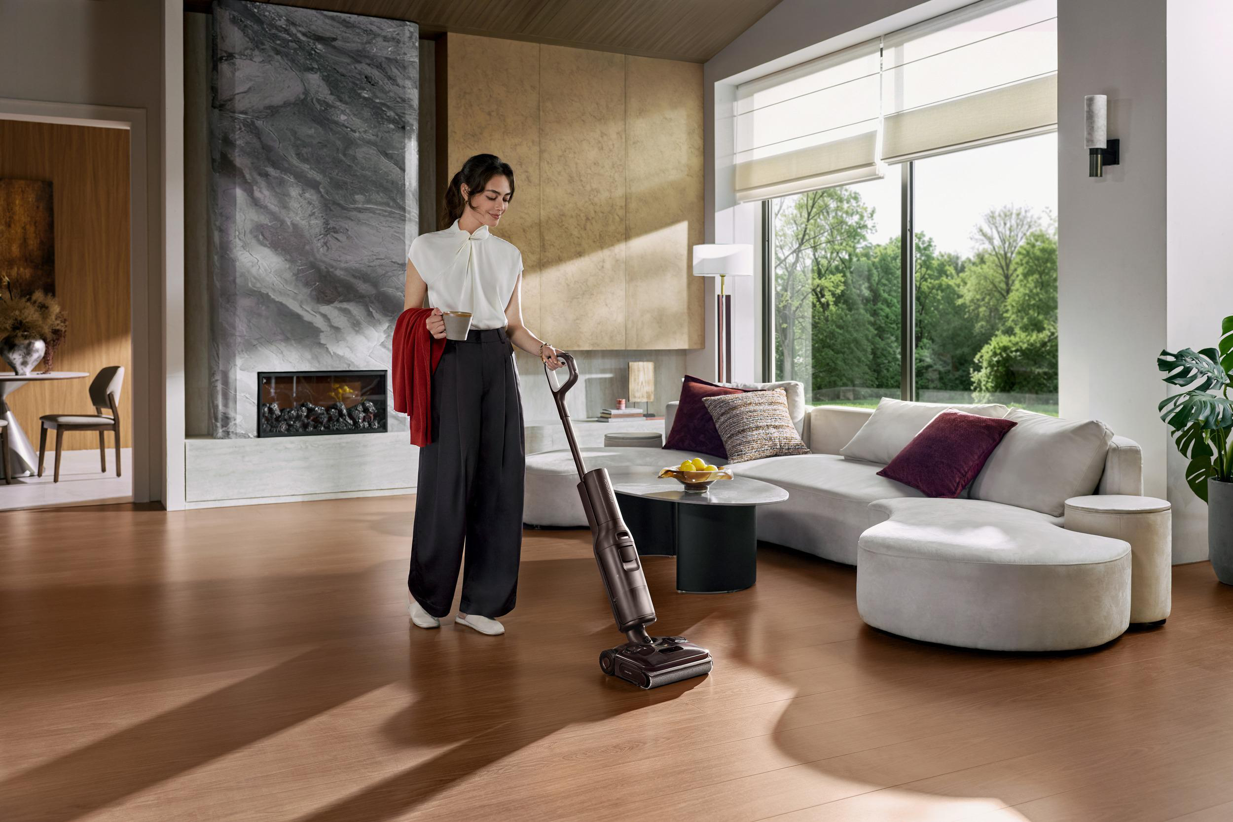 Eine Frau in moderner Kleidung bedient einen Staubsauger in einem hellen, eleganten Wohnzimmer.