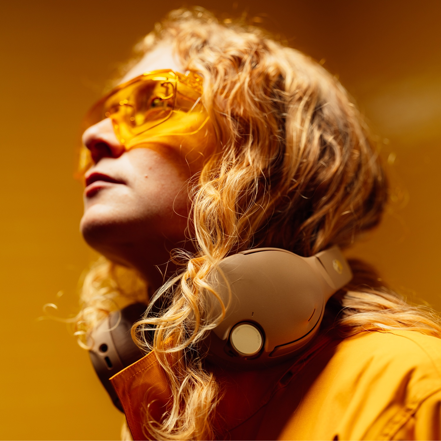 Une personne aux cheveux blonds, avec des lunettes de protection jaunes et un casque, regarde vers le haut.