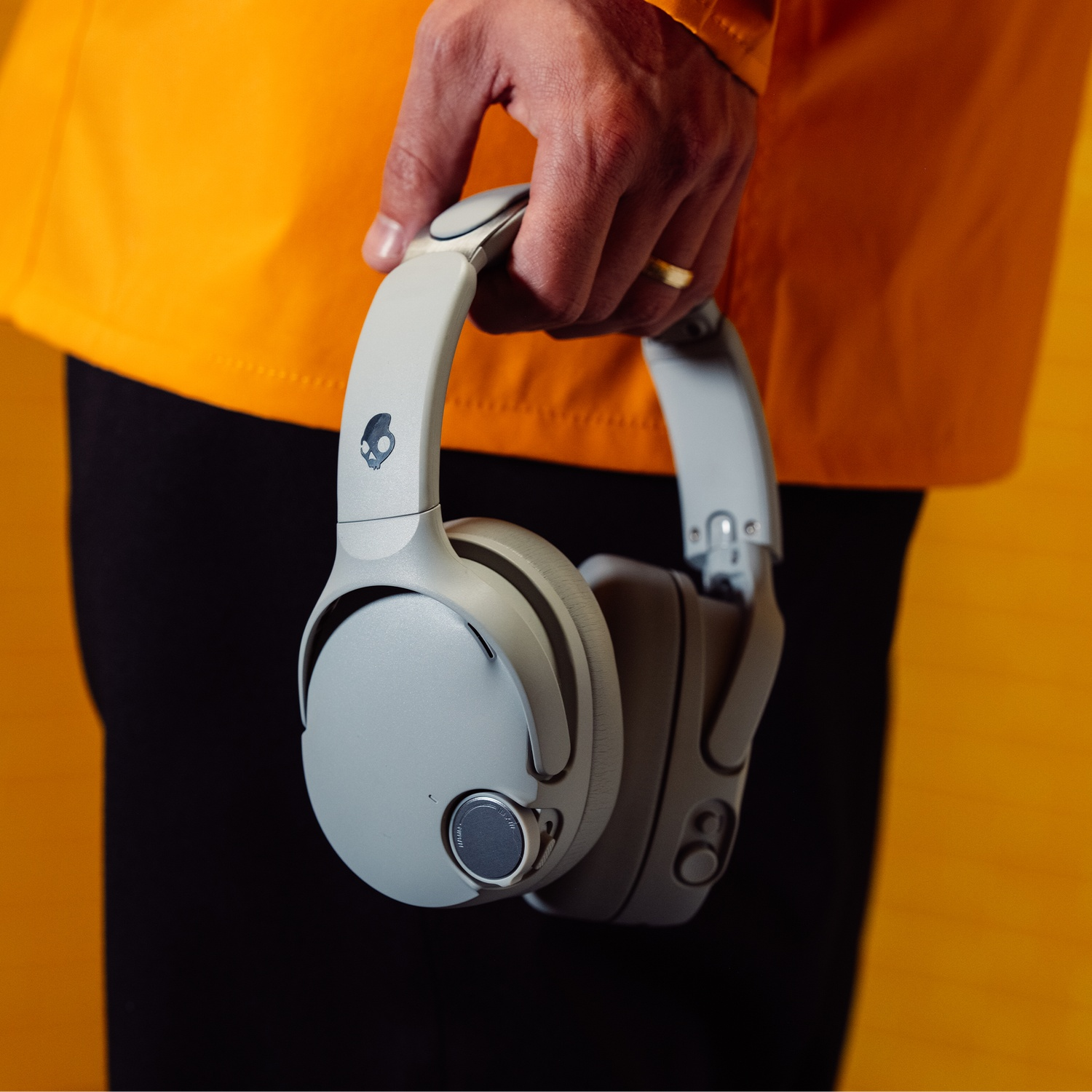 Une personne portant une veste orange tient un casque gris sur fond jaune.