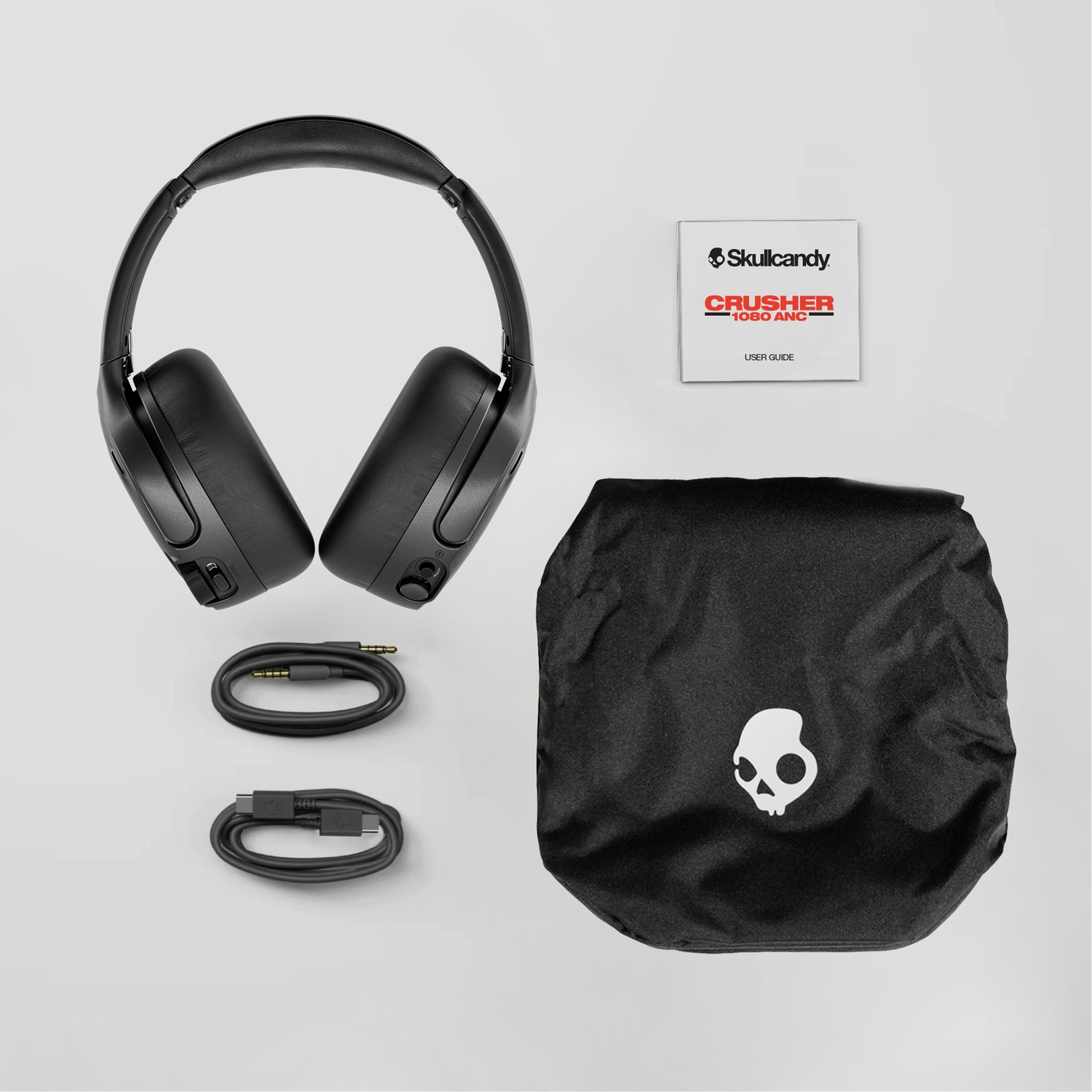 Casque Skullcandy noir, deux câbles, manuel d'utilisation et sac de transport sur fond gris.