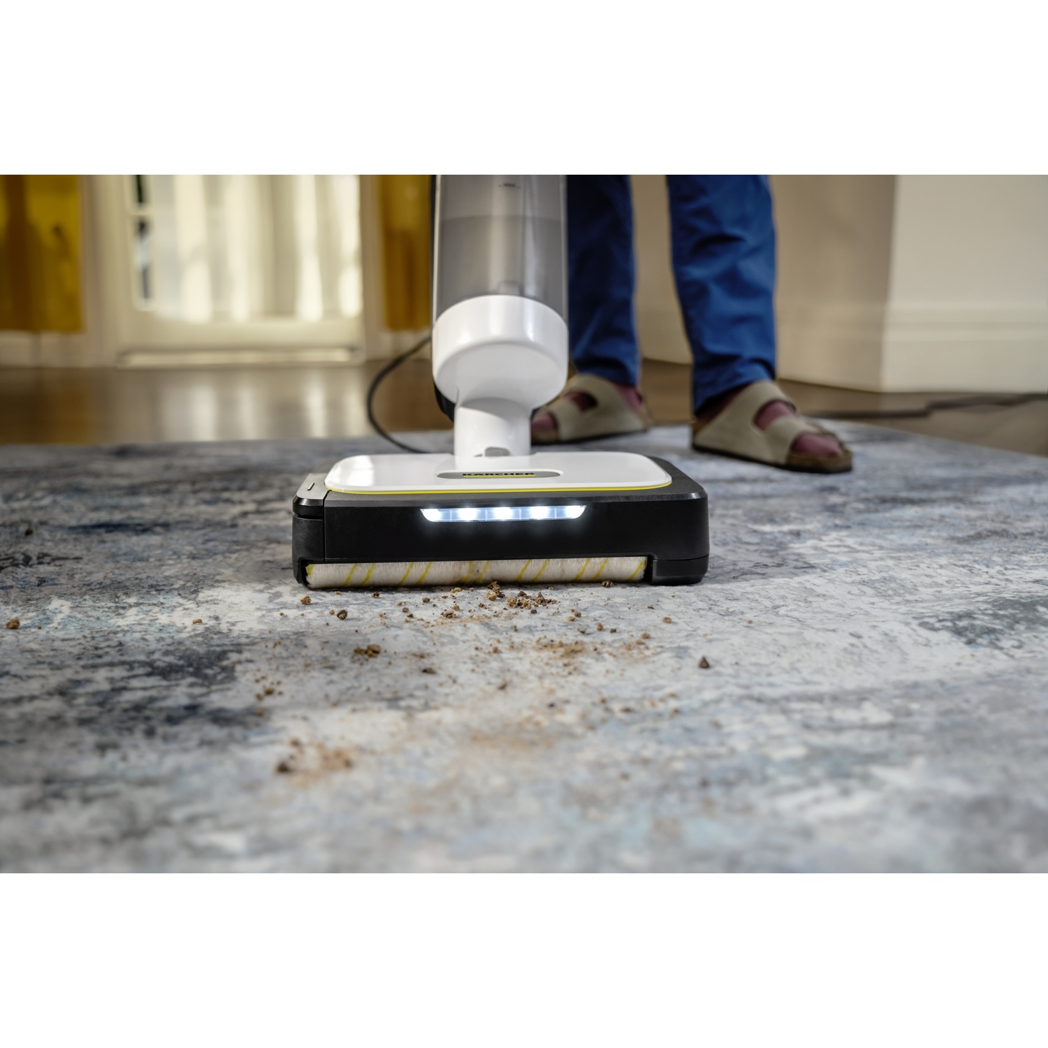 Un aspirateur blanc et noir nettoie la saleté d'un tapis bleu à l'intérieur.