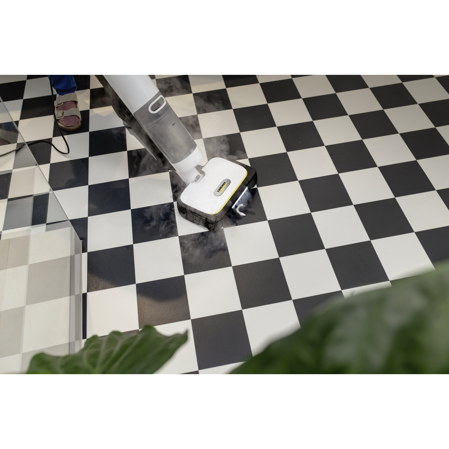 Un nettoyeur vapeur Karcher lave un sol à damier noir et blanc en dégageant de la vapeur.
