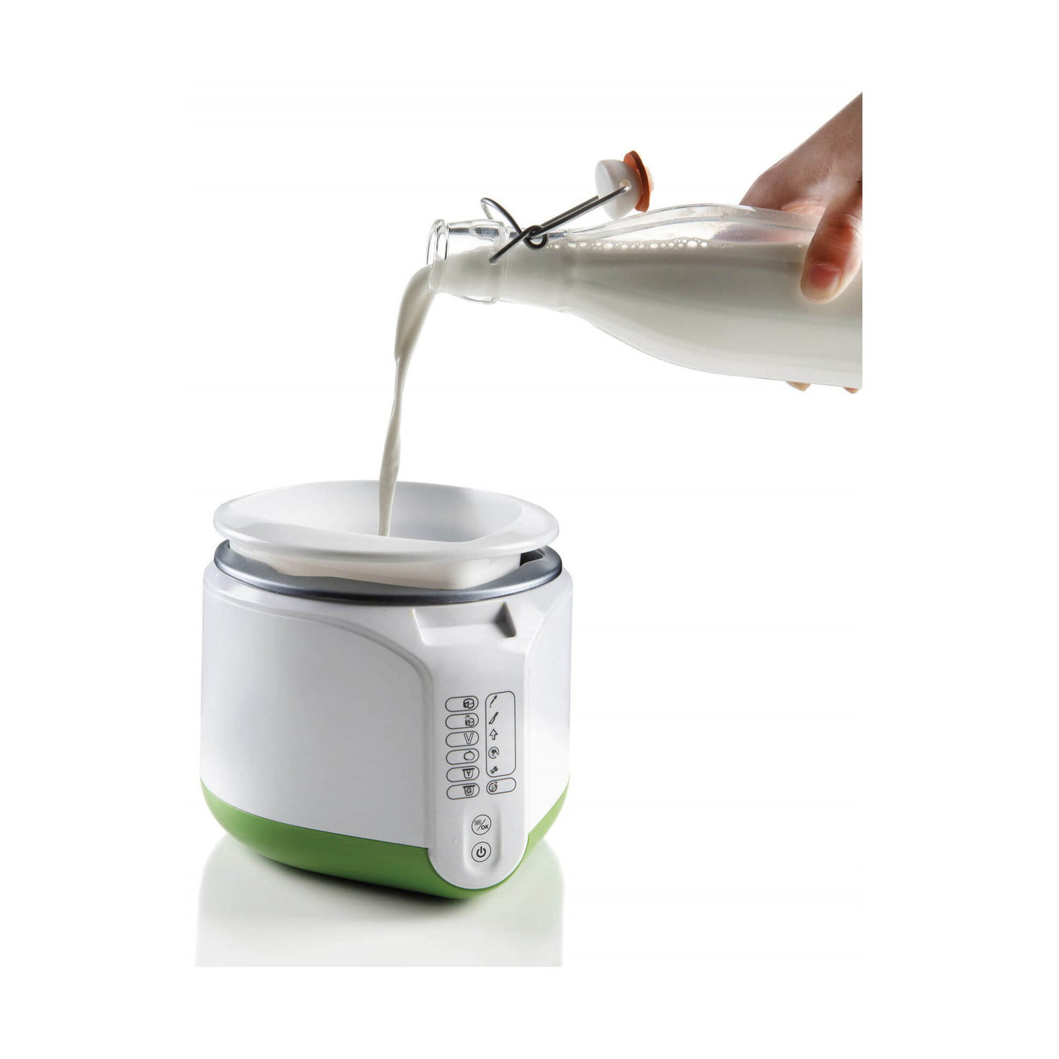 Una mano versa del latte da una bottiglia di vetro in una yogurtiera bianca e verde.