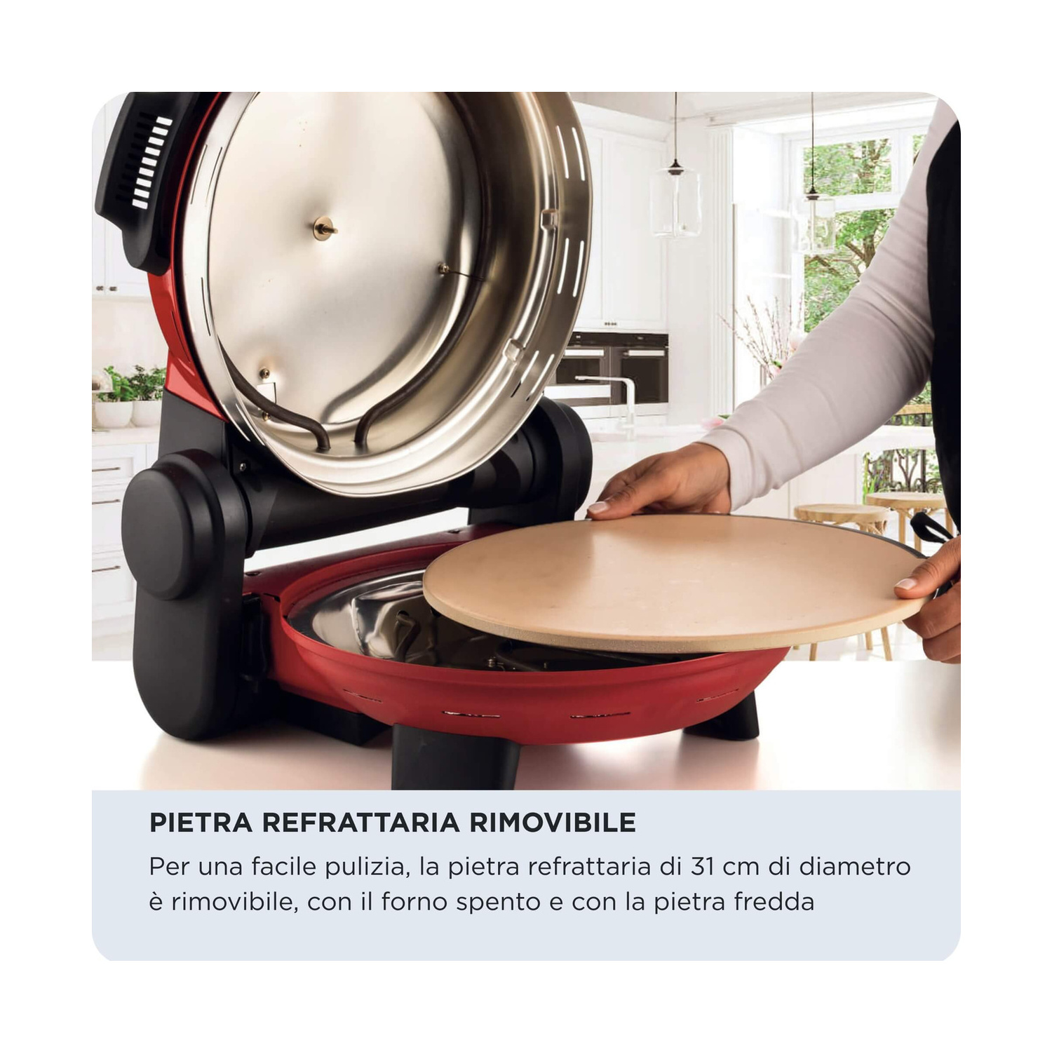 Una persona posiziona una pietra refrattaria rotonda nella base aperta di un forno rosso. Cucina luminosa sullo sfondo.