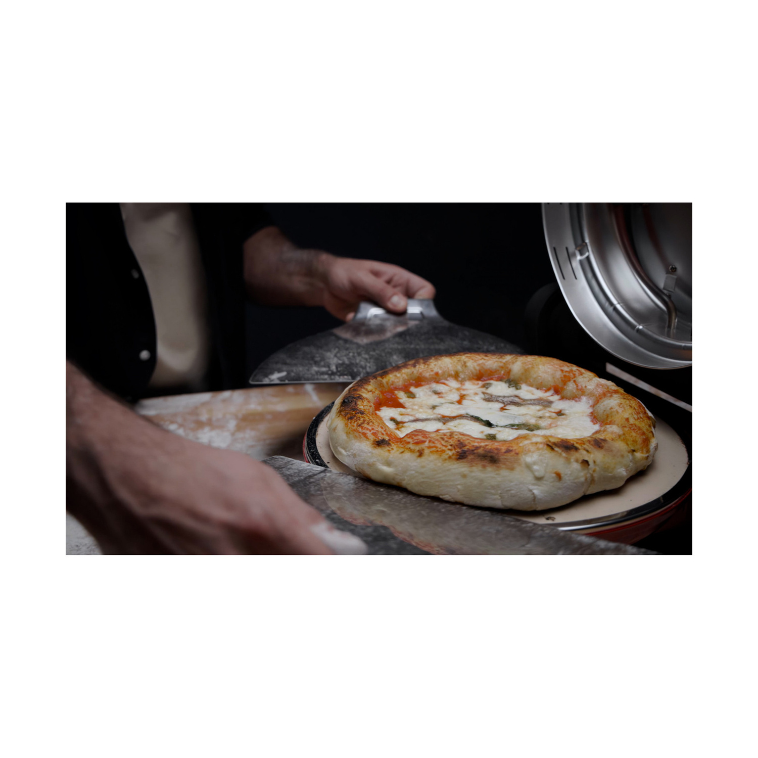 Una persona usa una pala di metallo per infornare una pizza appena sfornata con formaggio e pomodoro.