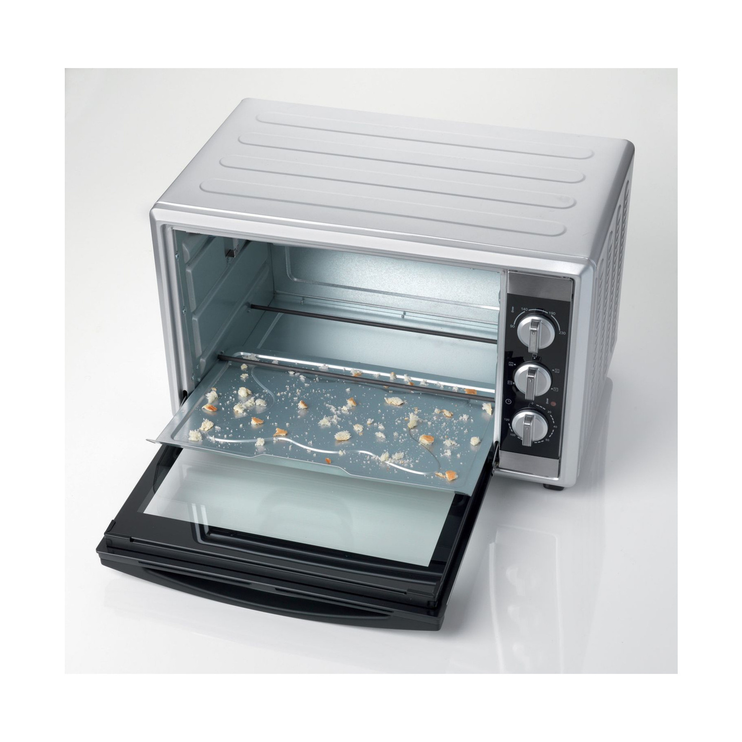 Un mini forno argentato con la porta aperta e briciole di pane sulla teglia su sfondo bianco.