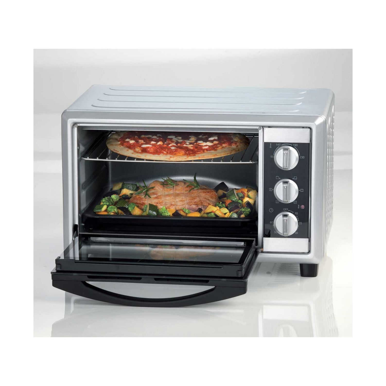 Un mini forno argentato con la porta aperta, che cuoce una pizza sopra e carne con verdure sotto.
