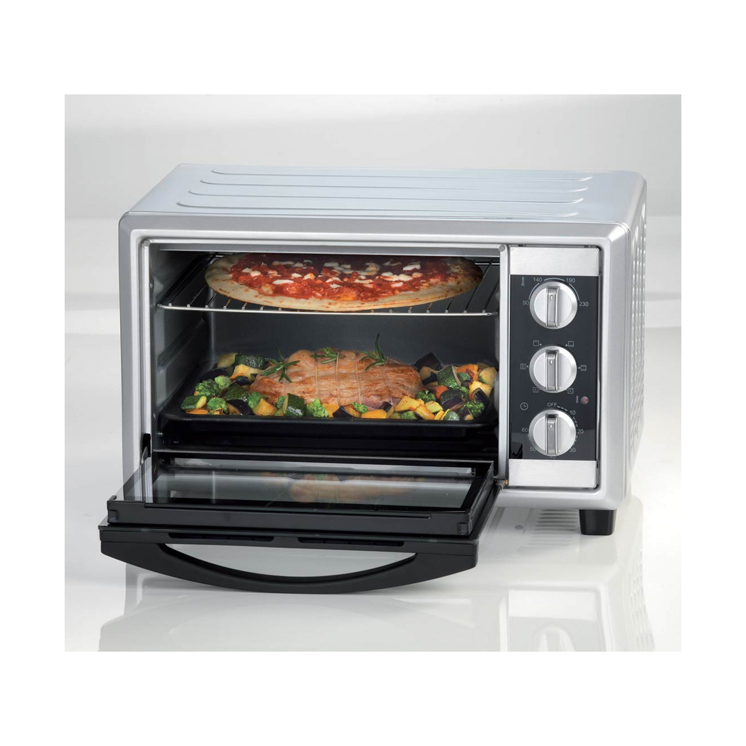Un mini forno argento con la porta aperta, che cuoce una pizza e carne con verdure.