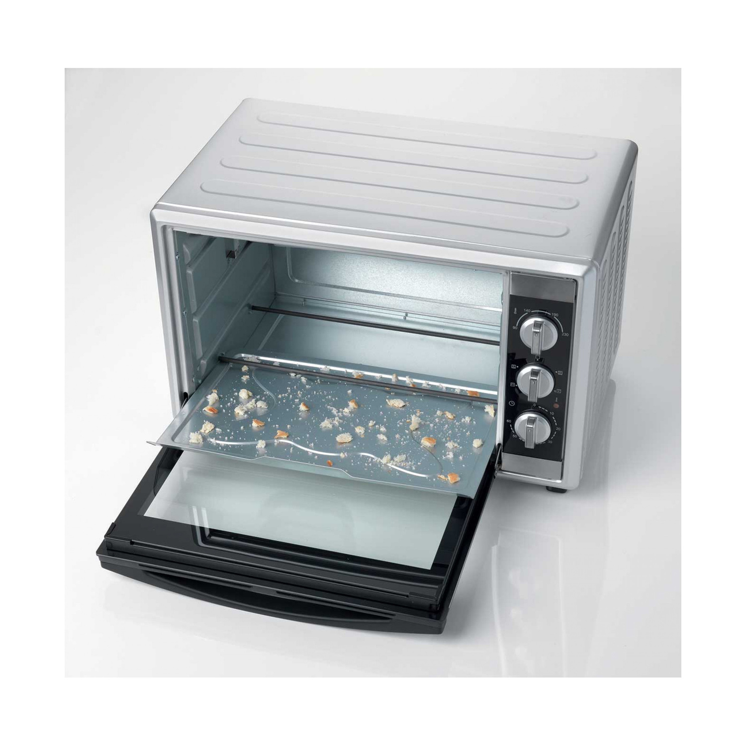 Un mini forno argentato con porta aperta e teglia piena di briciole su sfondo bianco.