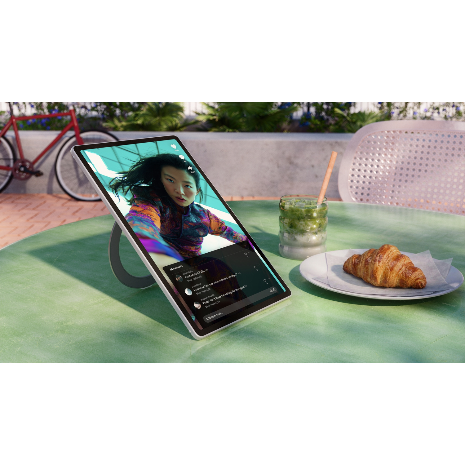 Un tablet con un video, un croissant e una bibita su un tavolo all'aperto.