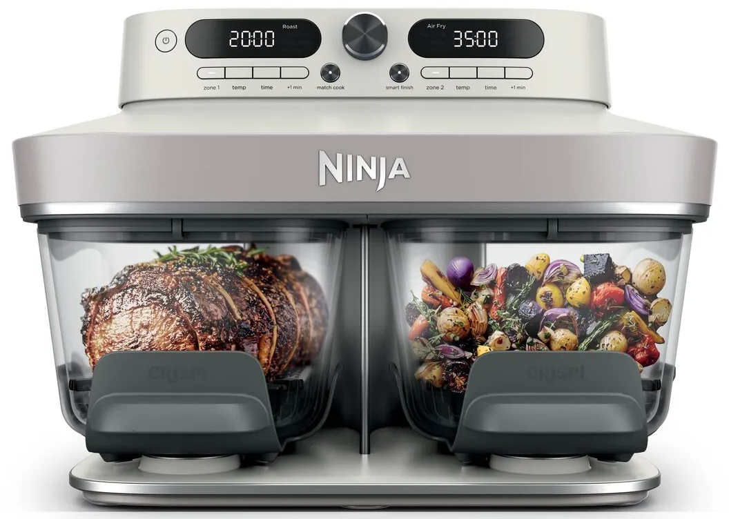 Eine weiße Ninja-Heißluftfritteuse mit zwei transparenten Körben, Fleisch links und Gemüse rechts.