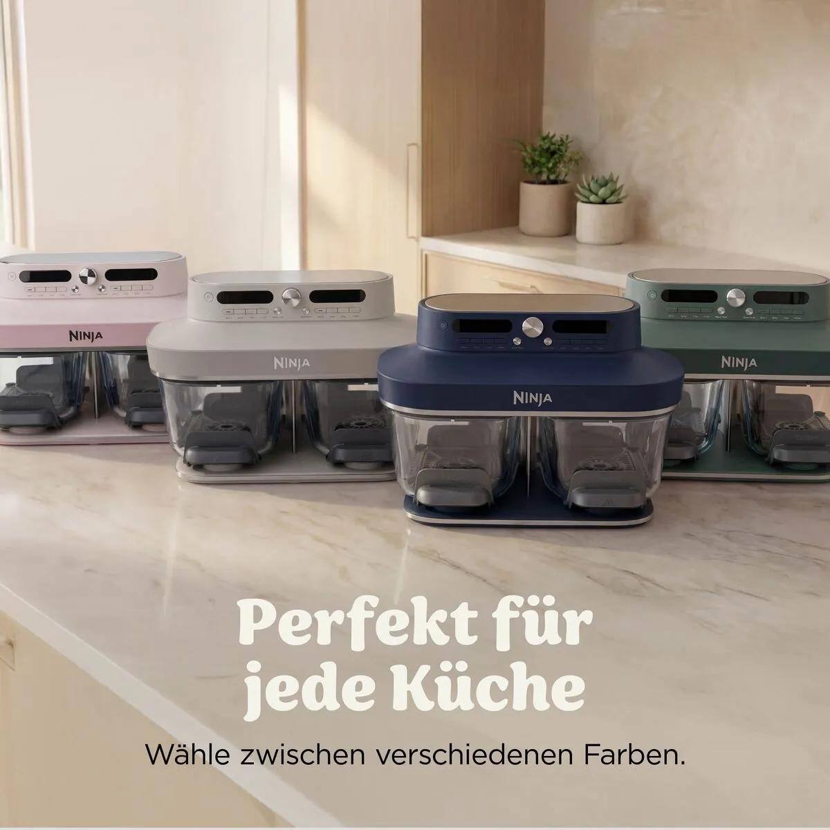 Vier Ninja Küchengeräte in Pink, Grau, Blau und Grün stehen auf einer Marmorarbeitsplatte in einer modernen Küche.