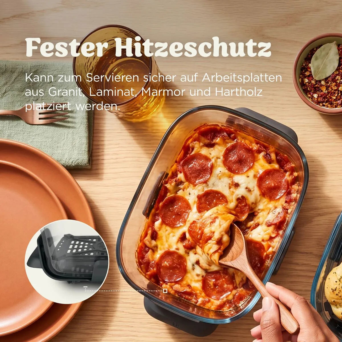 Auflauf mit Peperoni in einer Glasform, serviert auf Holz. Ein Löffel hebt ein Stück heraus.
