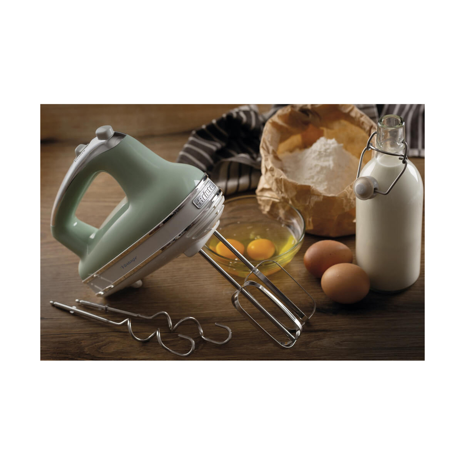 Un mixer a mano verde menta su un tavolo di legno con farina, uova, bottiglia di latte e accessori.