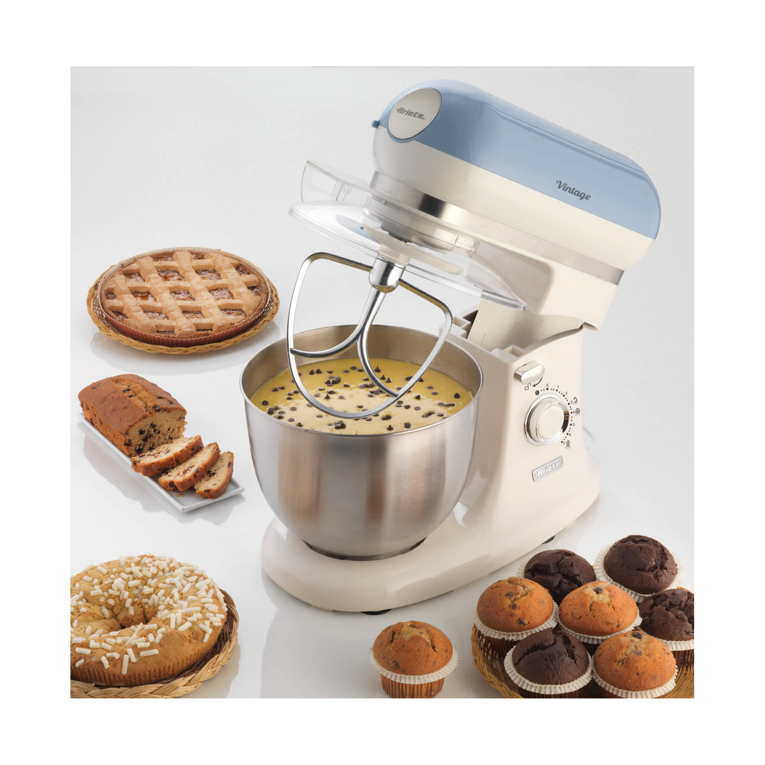 Impastatrice beige e blu con una ciotola di impasto, circondata da torte, muffin e dolci.